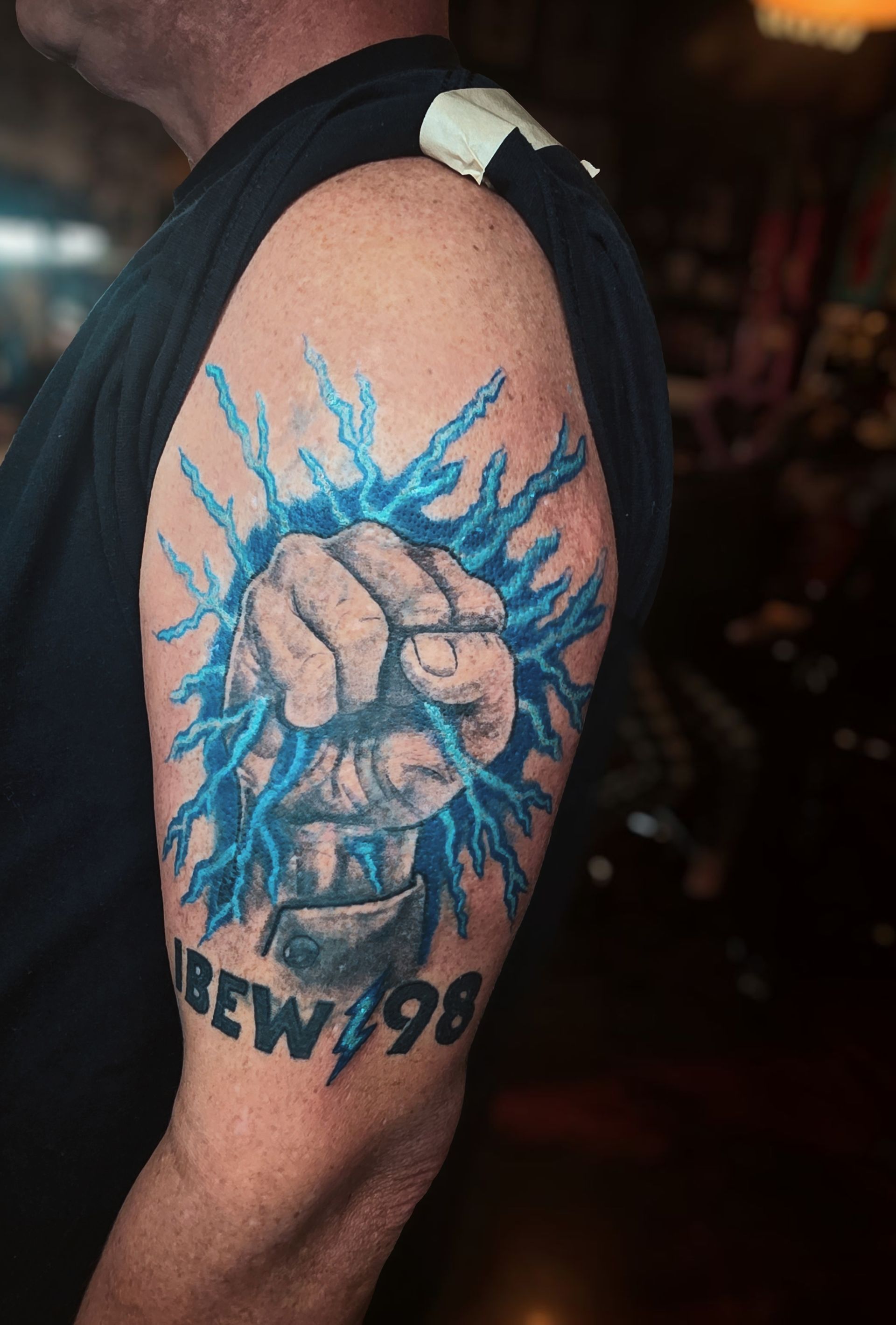 Tattoo of a clenched fist emerging from blue lightning. Text 
