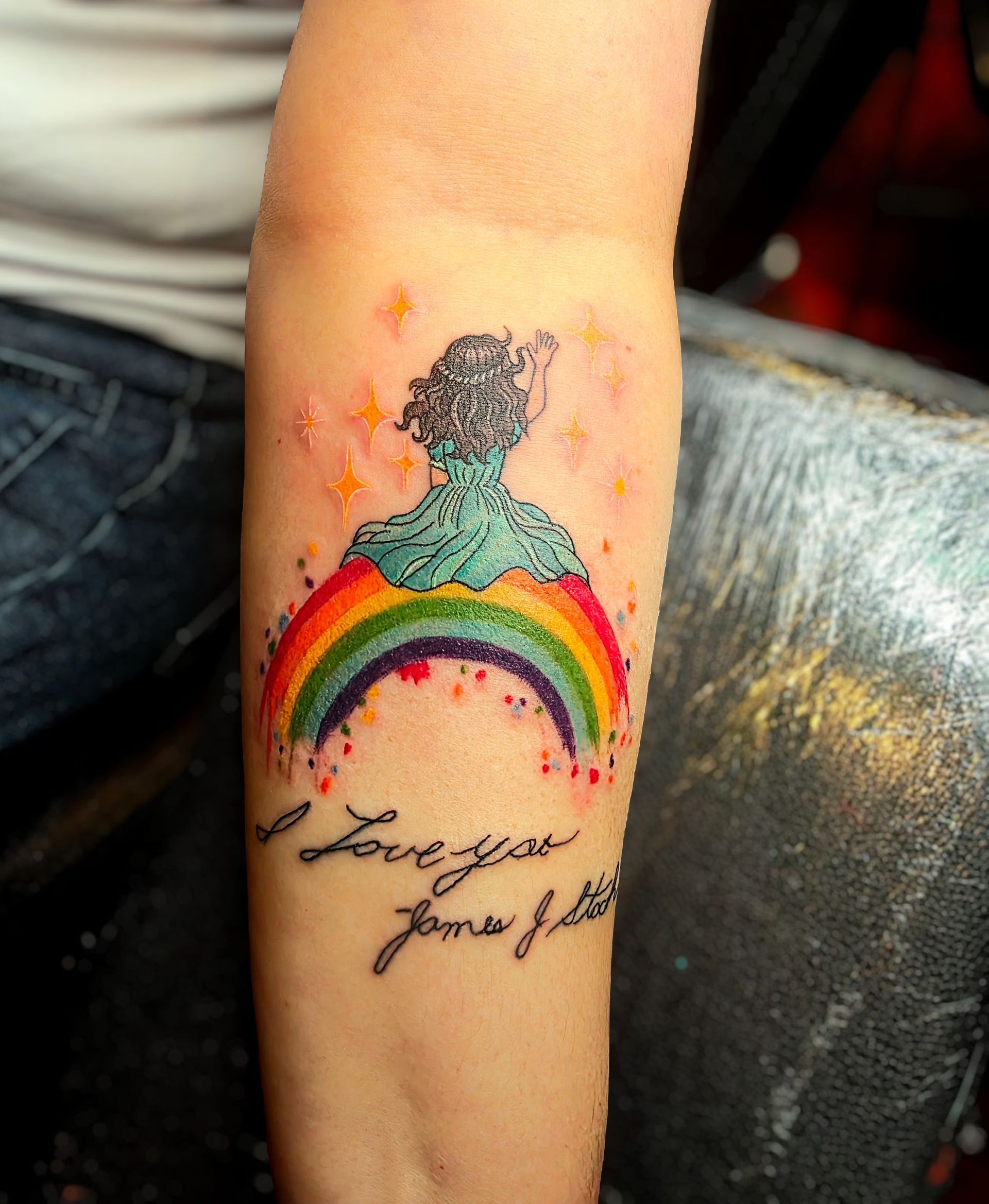 Colorful tattoo of person standing on a rainbow, text 