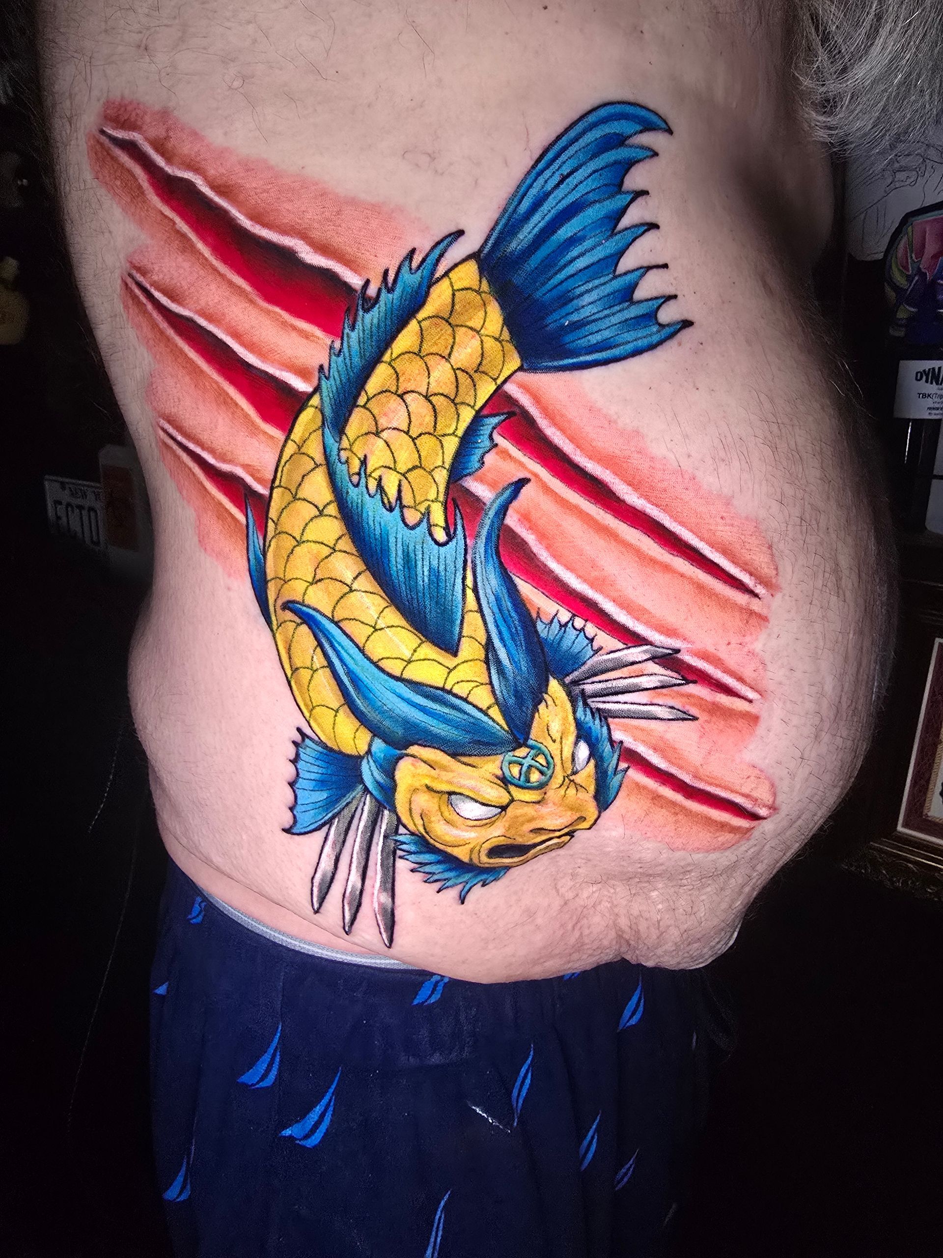 Tattoo of a yellow and blue fish with claw marks on the torso.