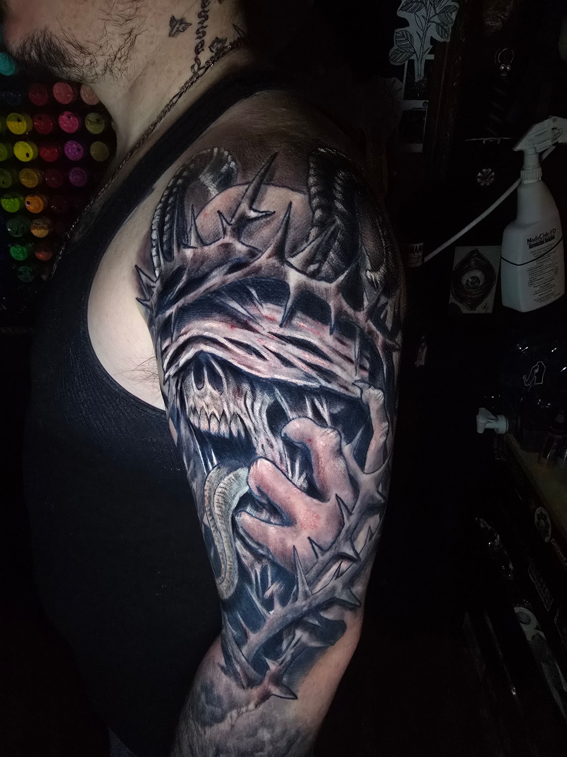 Tattoo on arm depicts a skull wearing a crown of thorns, reaching out, set in detailed shading.