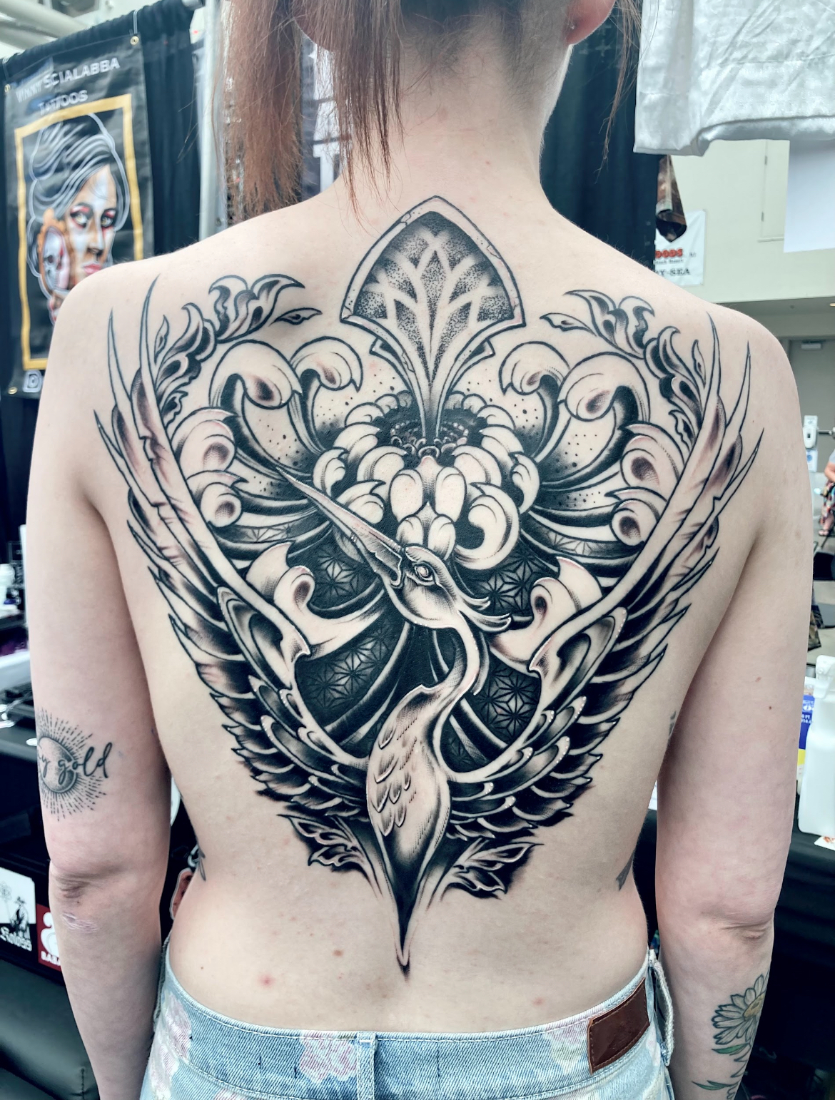 Tattoo of a heron with ornate wings and floral elements on a person's back.
