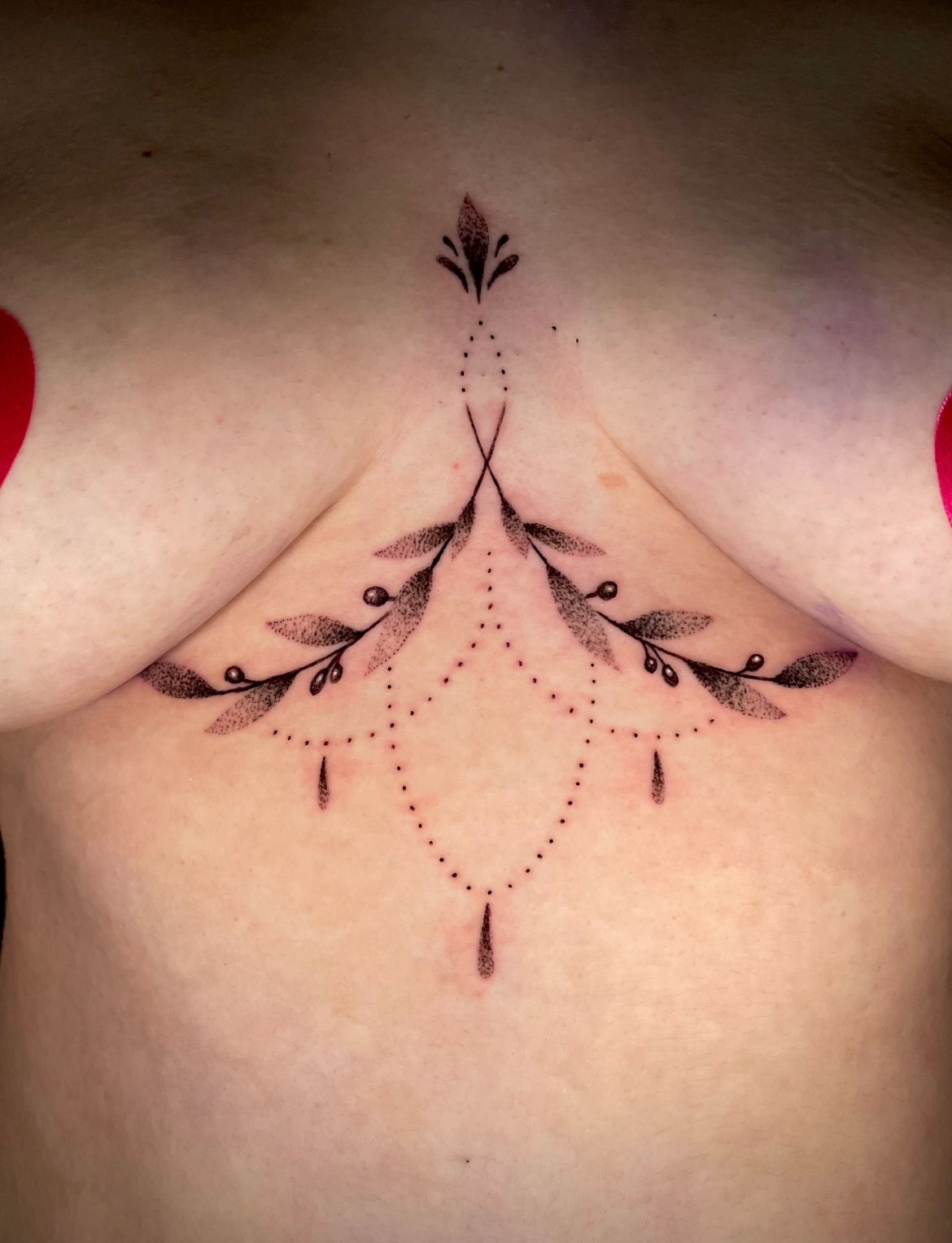 Chest tattoo: delicate floral design centered between breasts, with leaf and dot details.