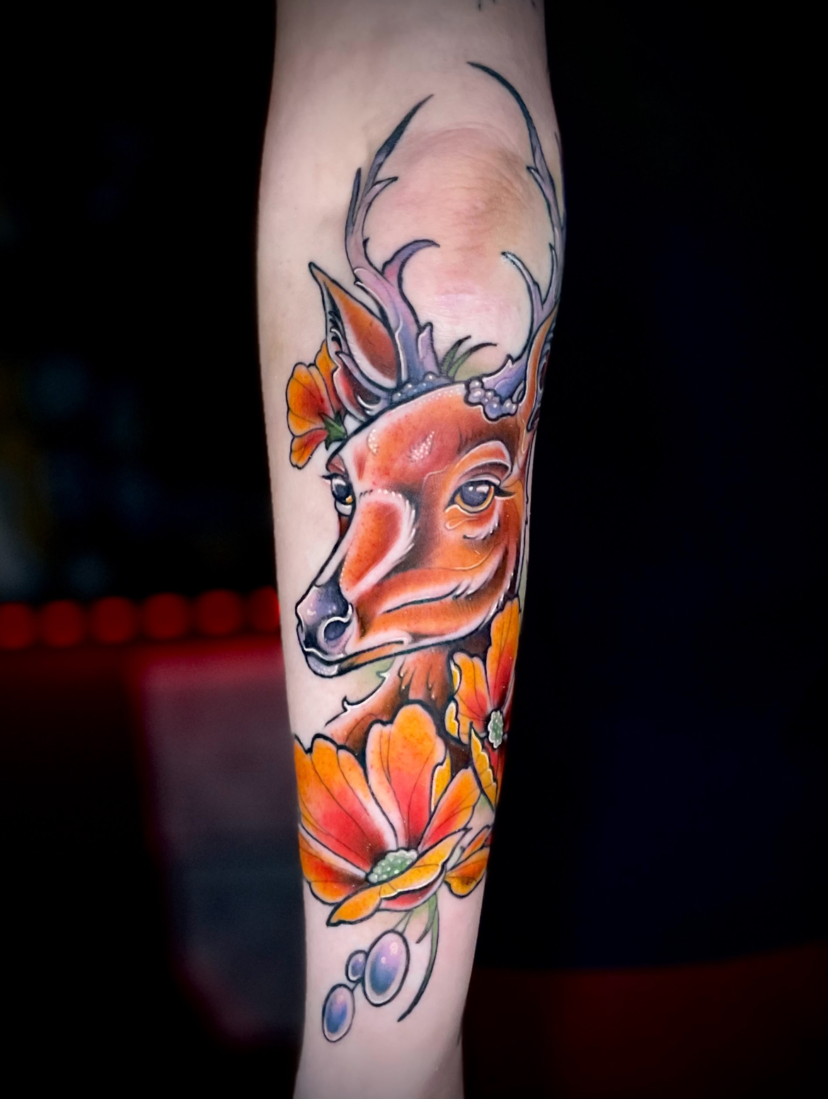 Deer head tattoo with orange flowers; dark background.