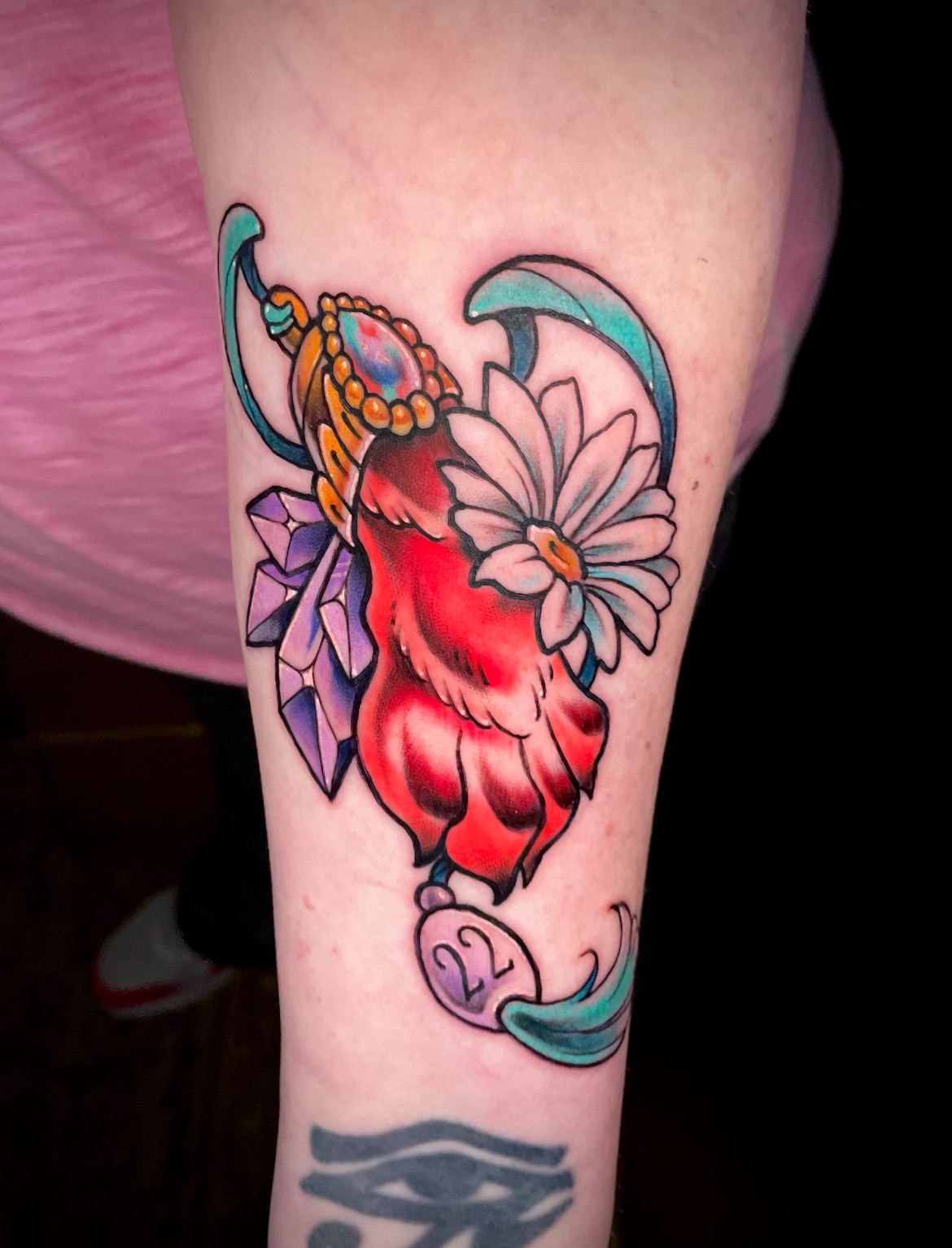 Tattoo of a red paw print with daisy, gemstones, and a decorative frame on arm.