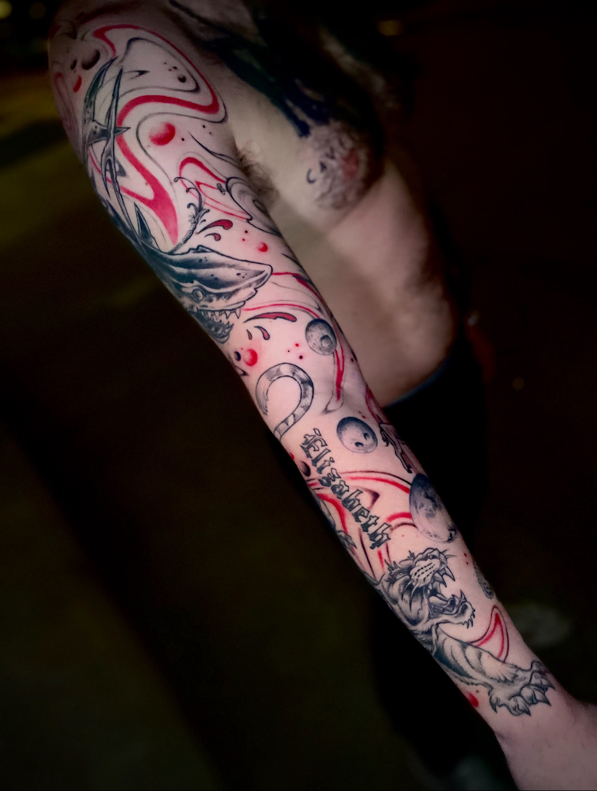 Arm tattoo with red and black abstract design featuring swirling lines and eye shapes.
