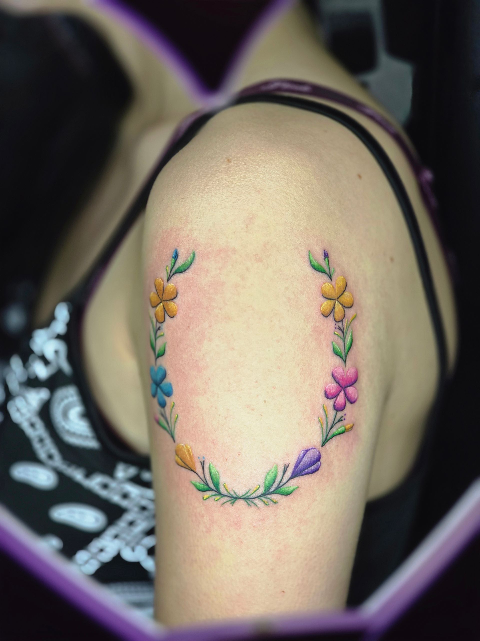 Colorful flower wreath tattoo on a person's shoulder.