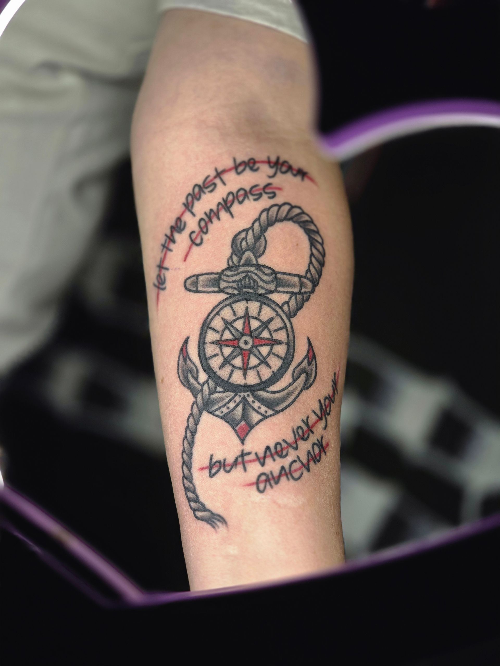 Tattoo of an anchor entwined with a compass and rope, with text 