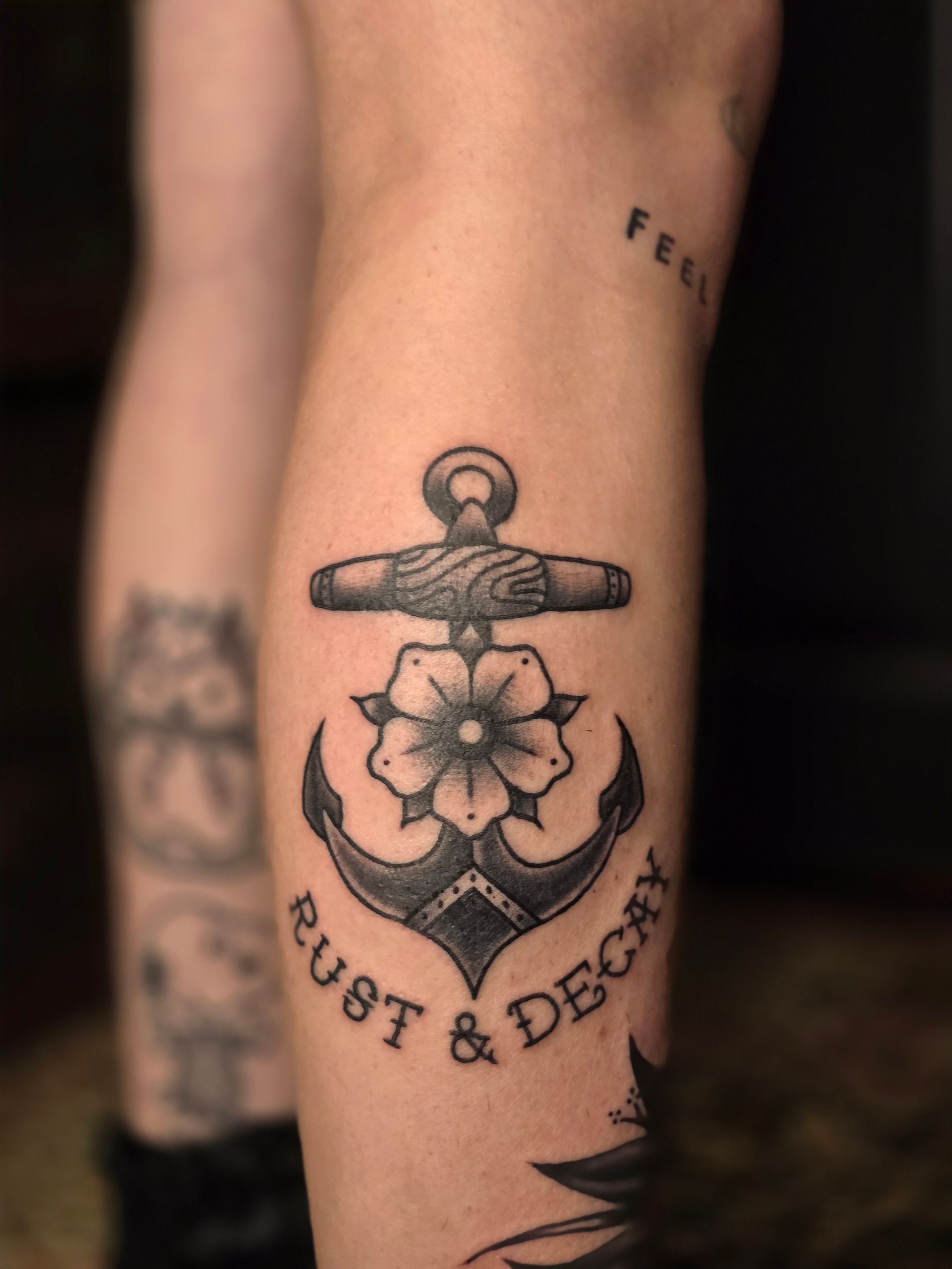 Black and white anchor tattoo with a flower, the words 