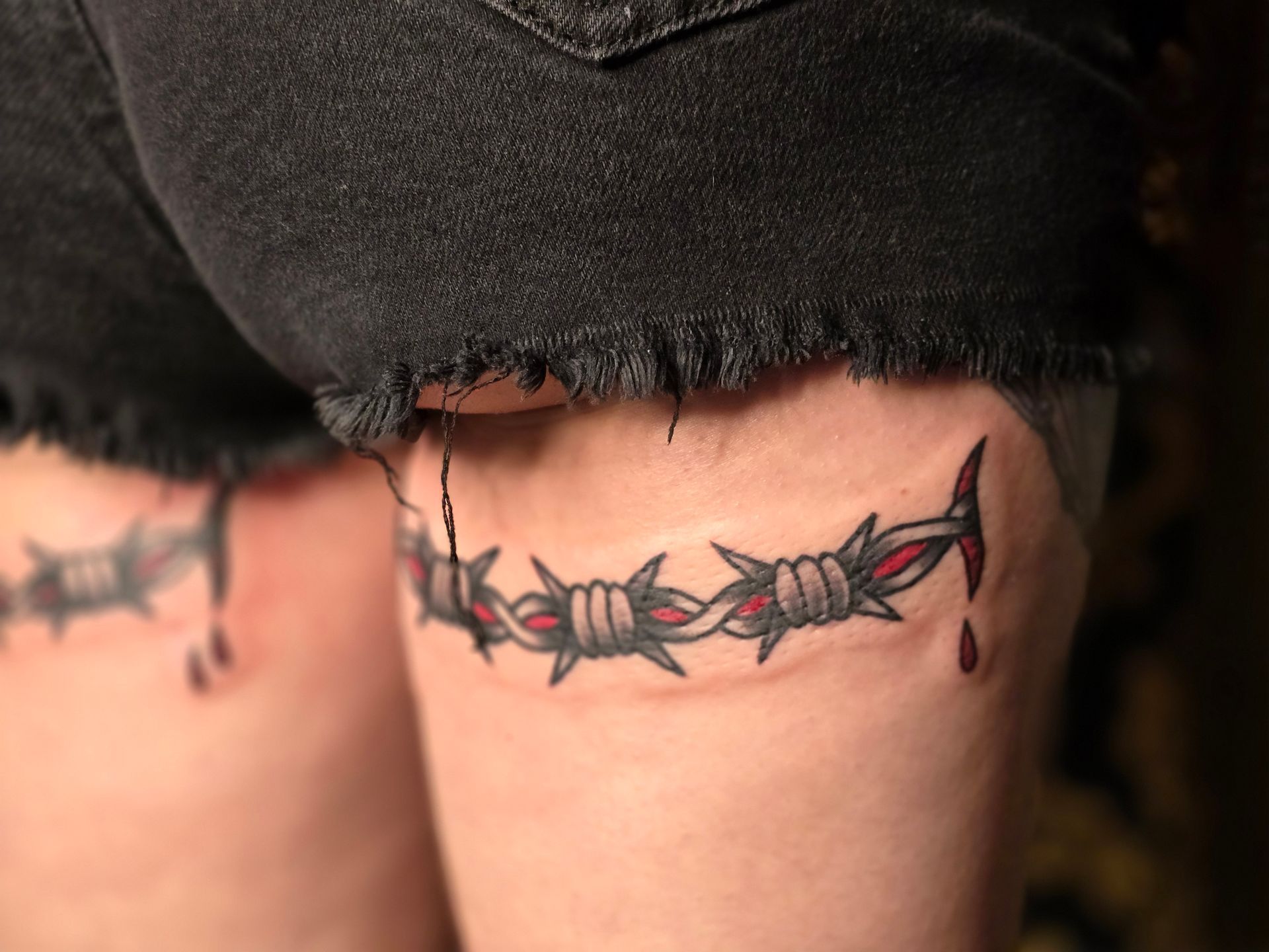 Barbed wire tattoo on a thigh, with red accents and blood drops.