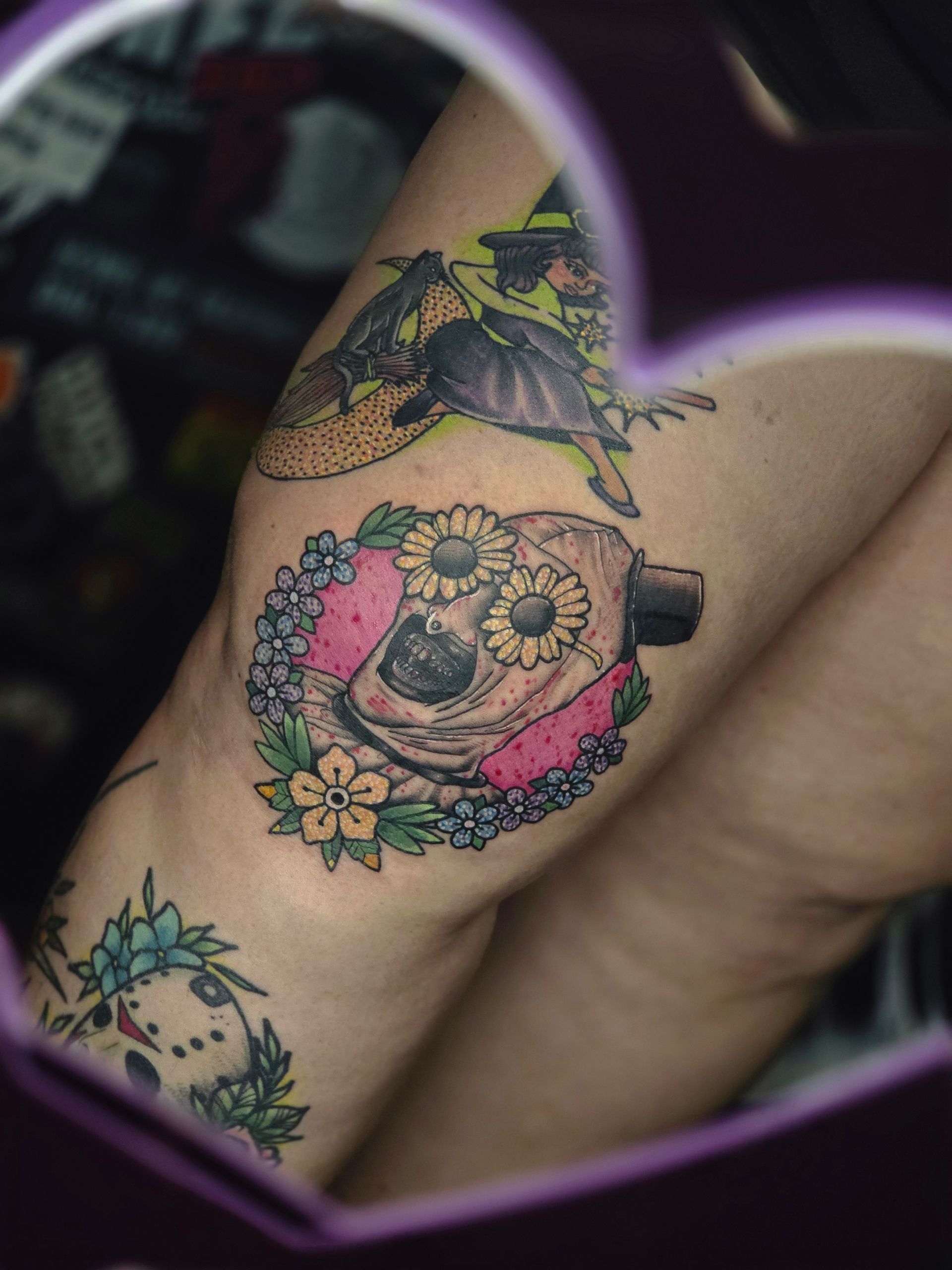 Tattoo of Jason Voorhees mask with flowers, witch, and another mask with flowers on a leg.