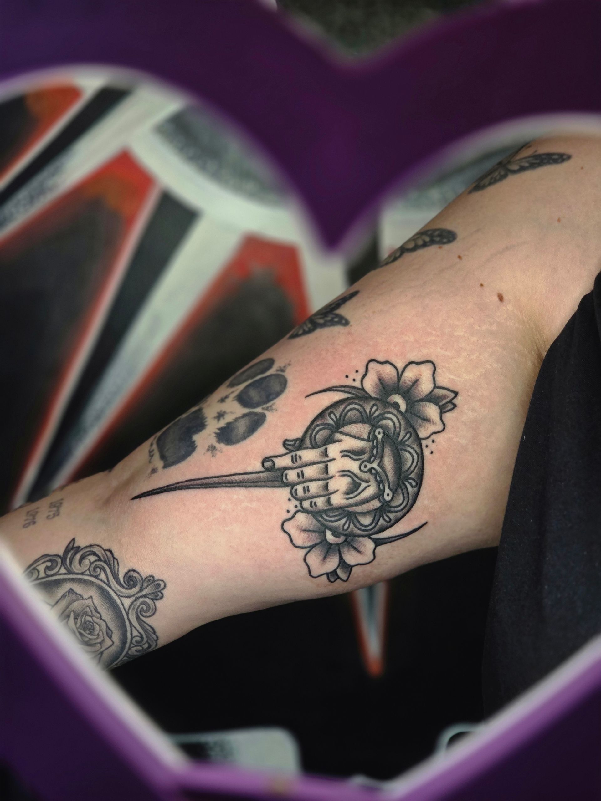 Arm tattoo: Hand of the King pin with floral accents.