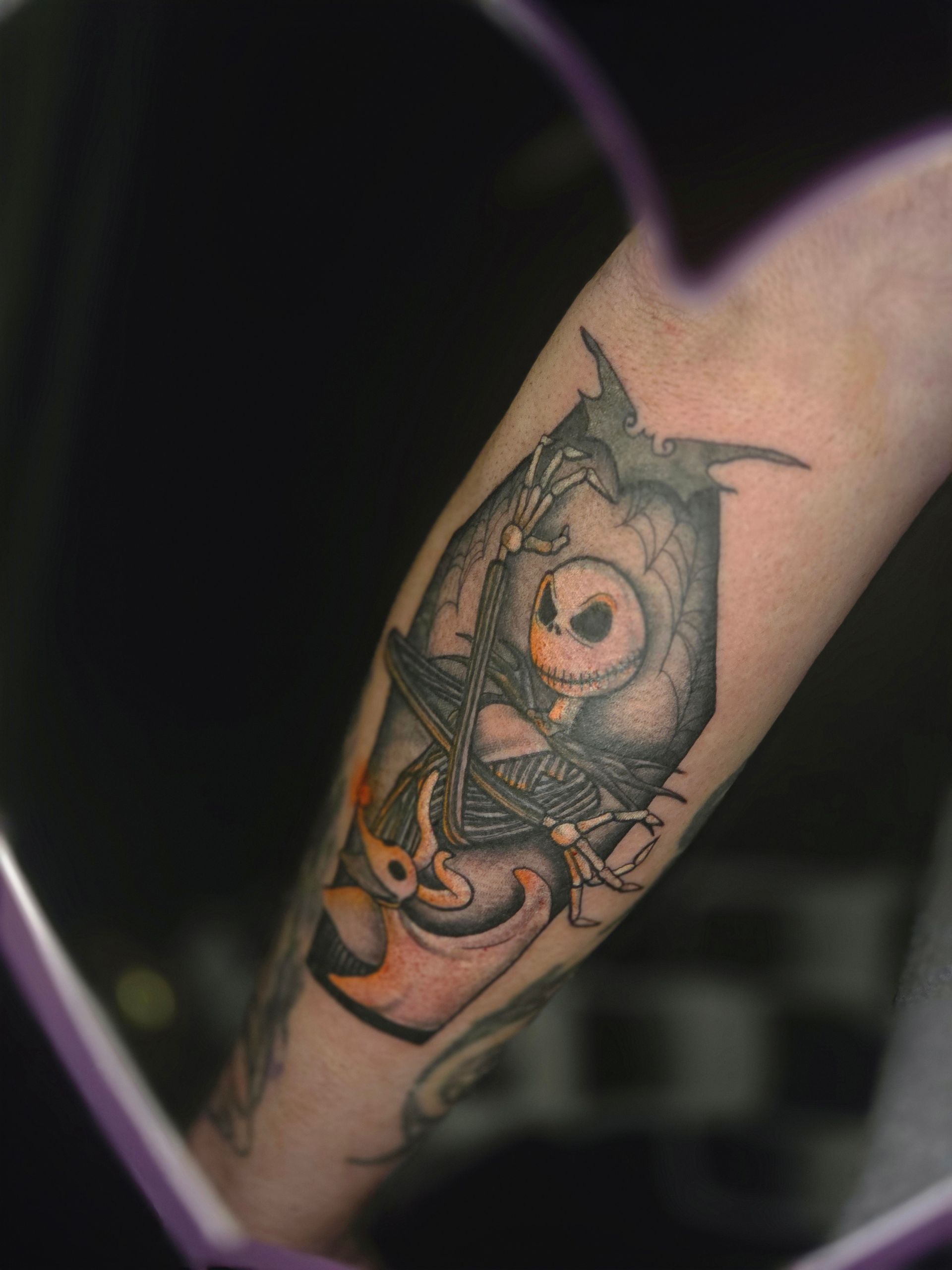 Tattoo on forearm depicts an owl in a coffin with Jack Skellington face and a flame.