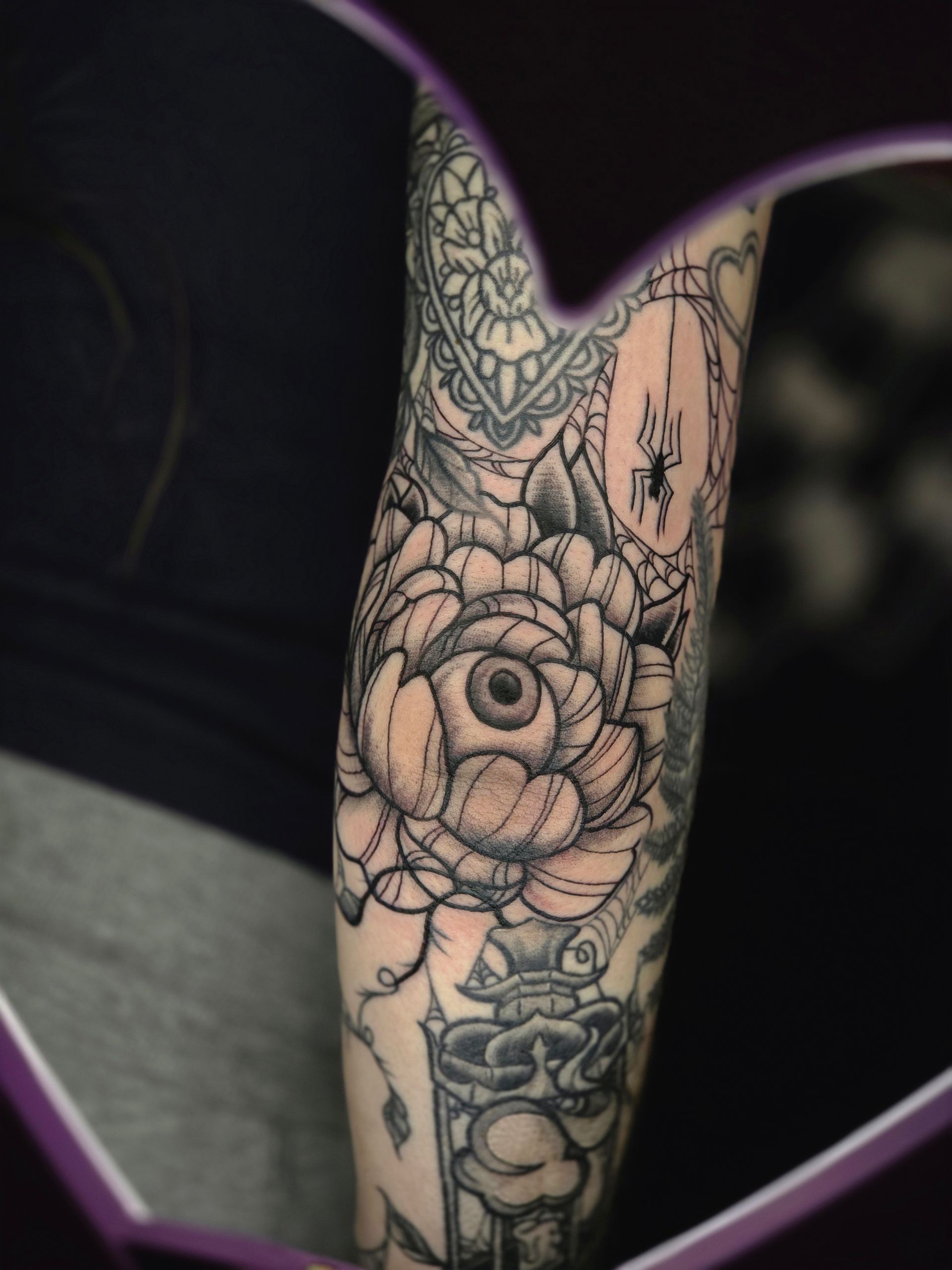 Black and white tattoo of an eye inside a flower, with other design elements on the arm.