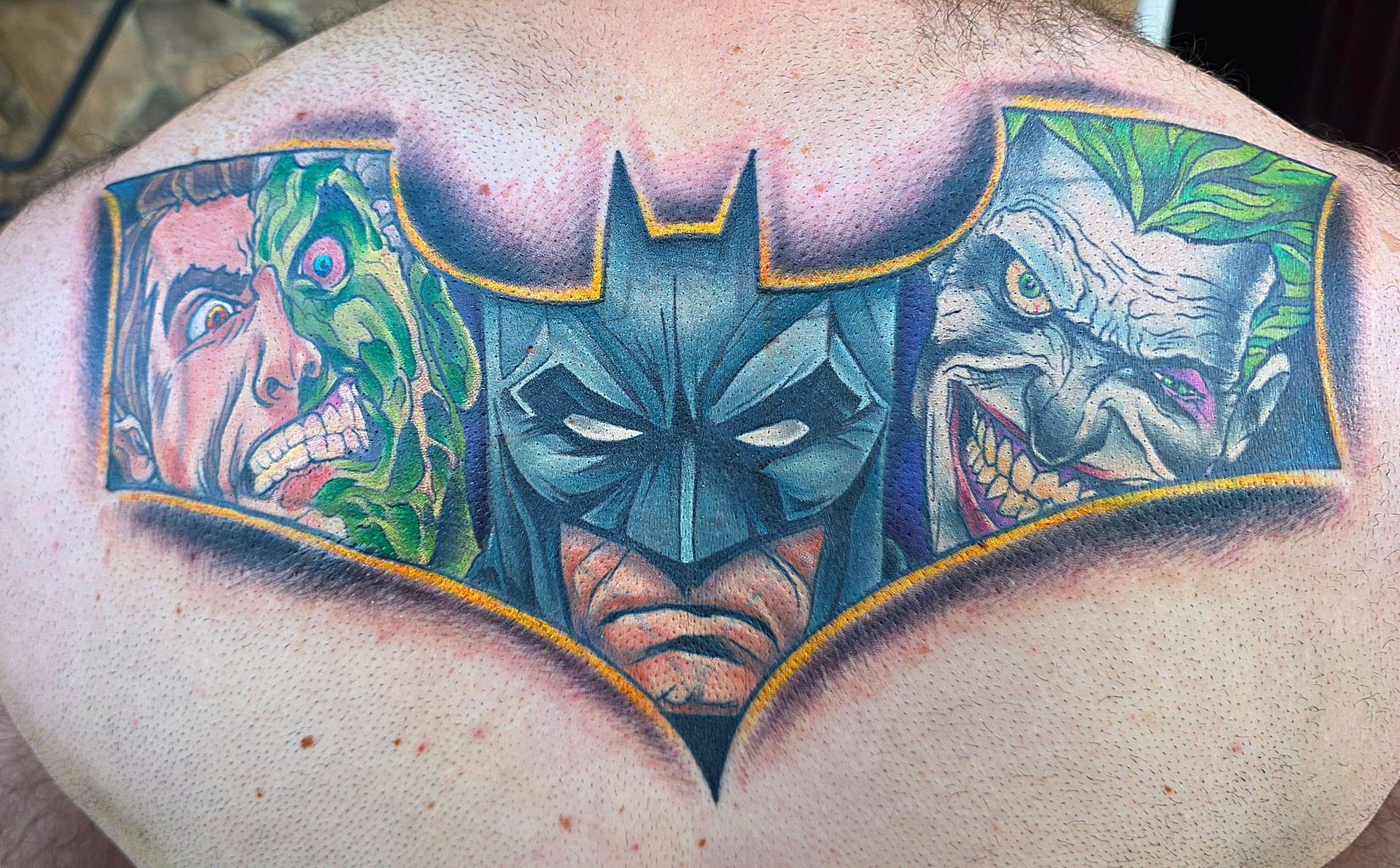 Batman tattoo on the back, featuring Batman with Two-Face and Joker on either side; colorful.