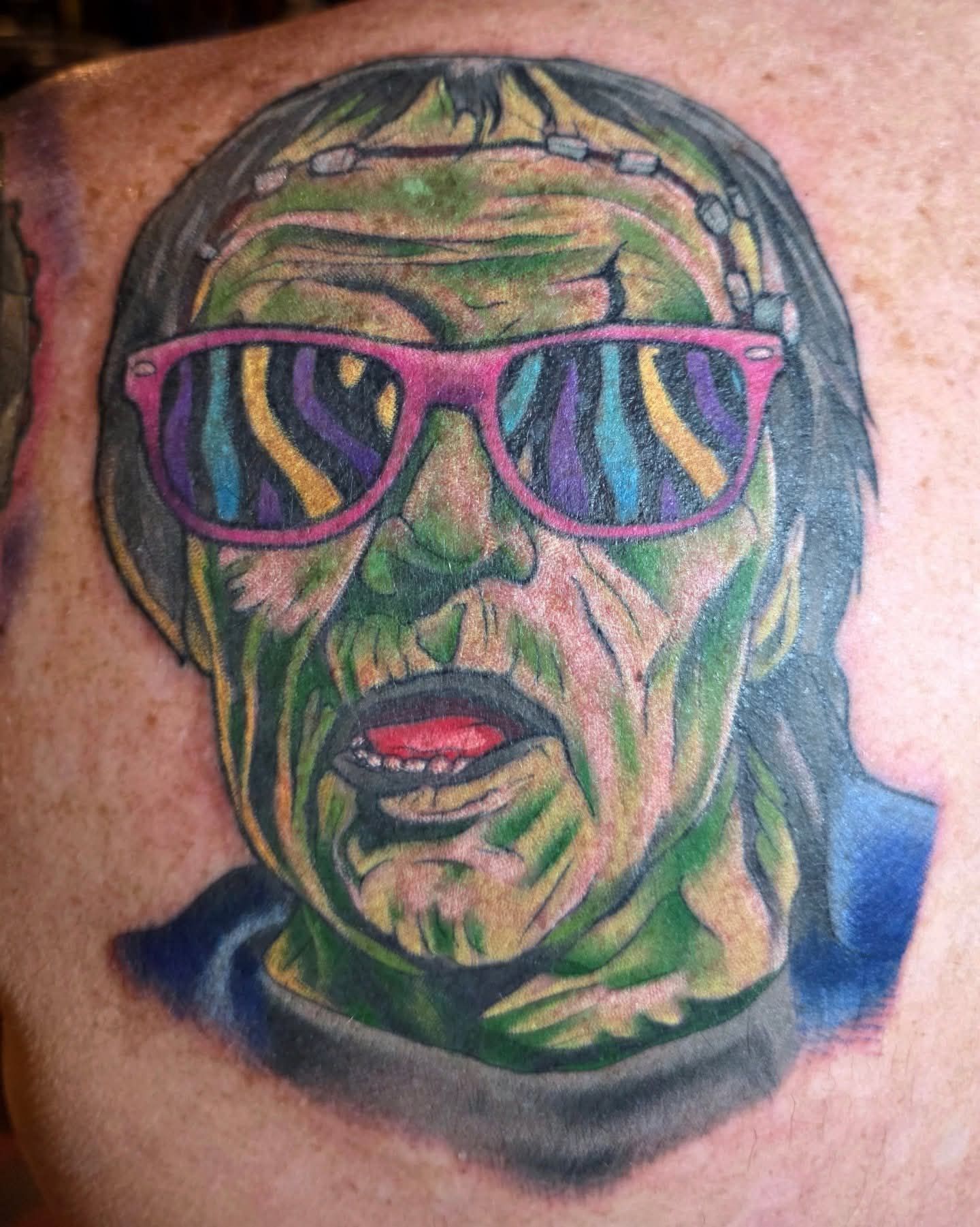 Tattoo of Frankenstein's monster wearing pink sunglasses with a psychedelic reflection. Green skin, gray hair.