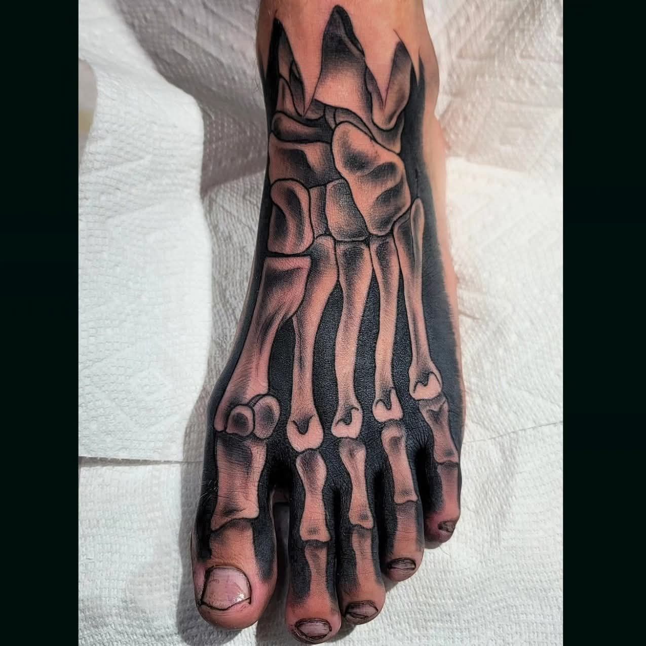 Foot tattoo depicting a skeletal foot in grayscale, centered on a white surface.