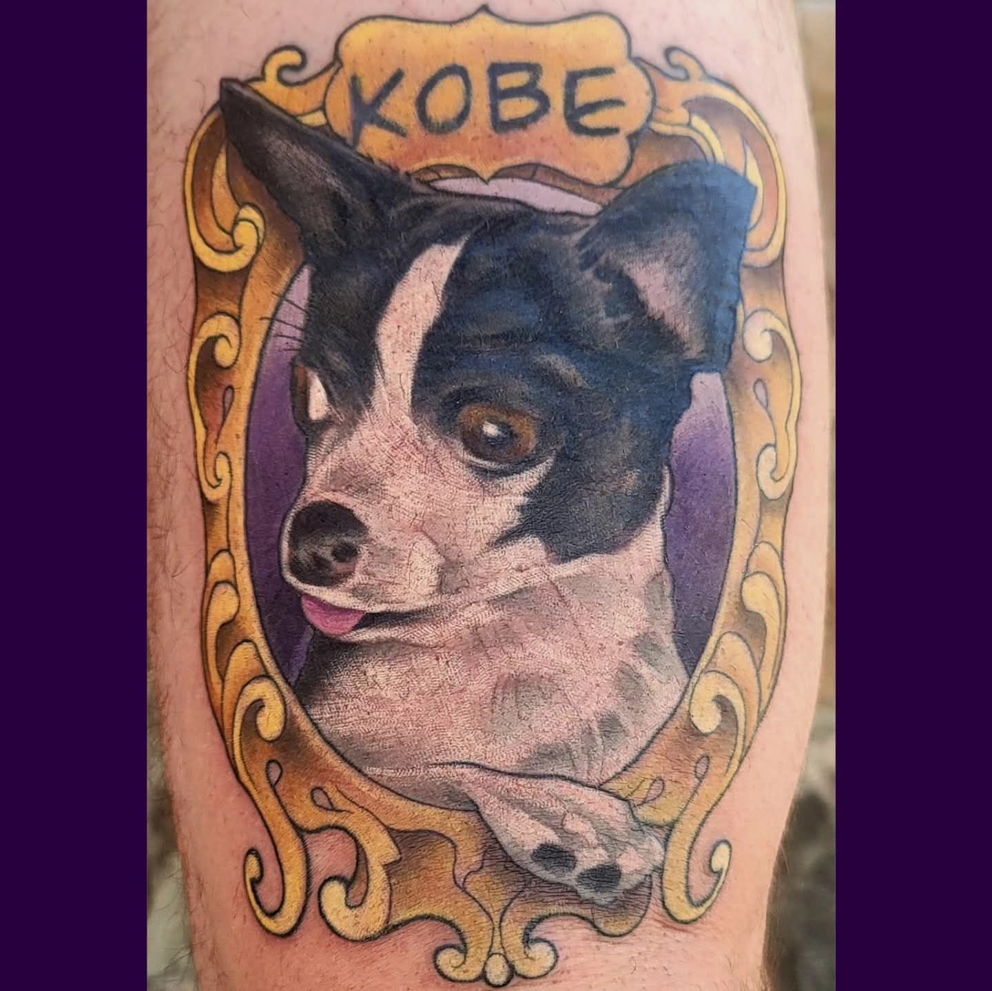 Tattoo of a black and white dog named Kobe in a gold ornate frame, with a purple background.