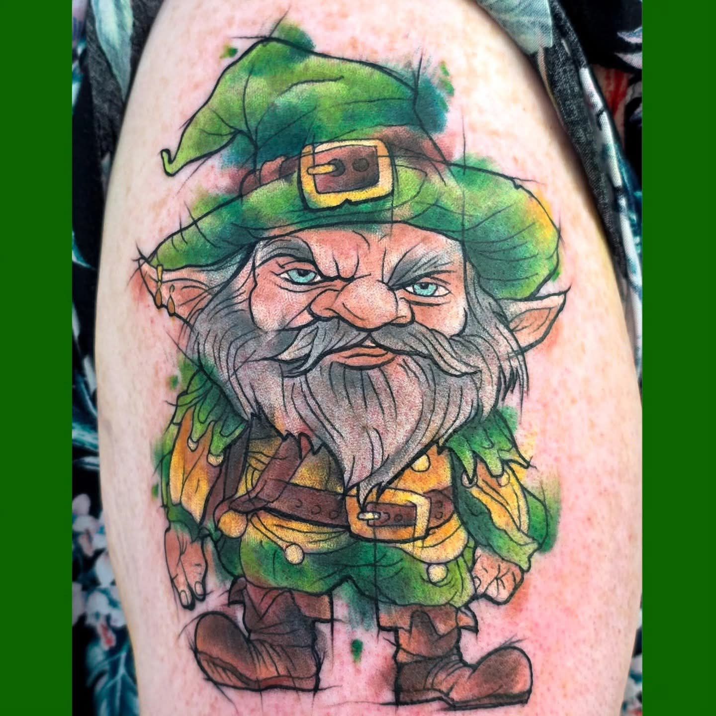Tattoo of an angry leprechaun in green and yellow clothing, green hat, gray beard and eyebrows, and stern expression.