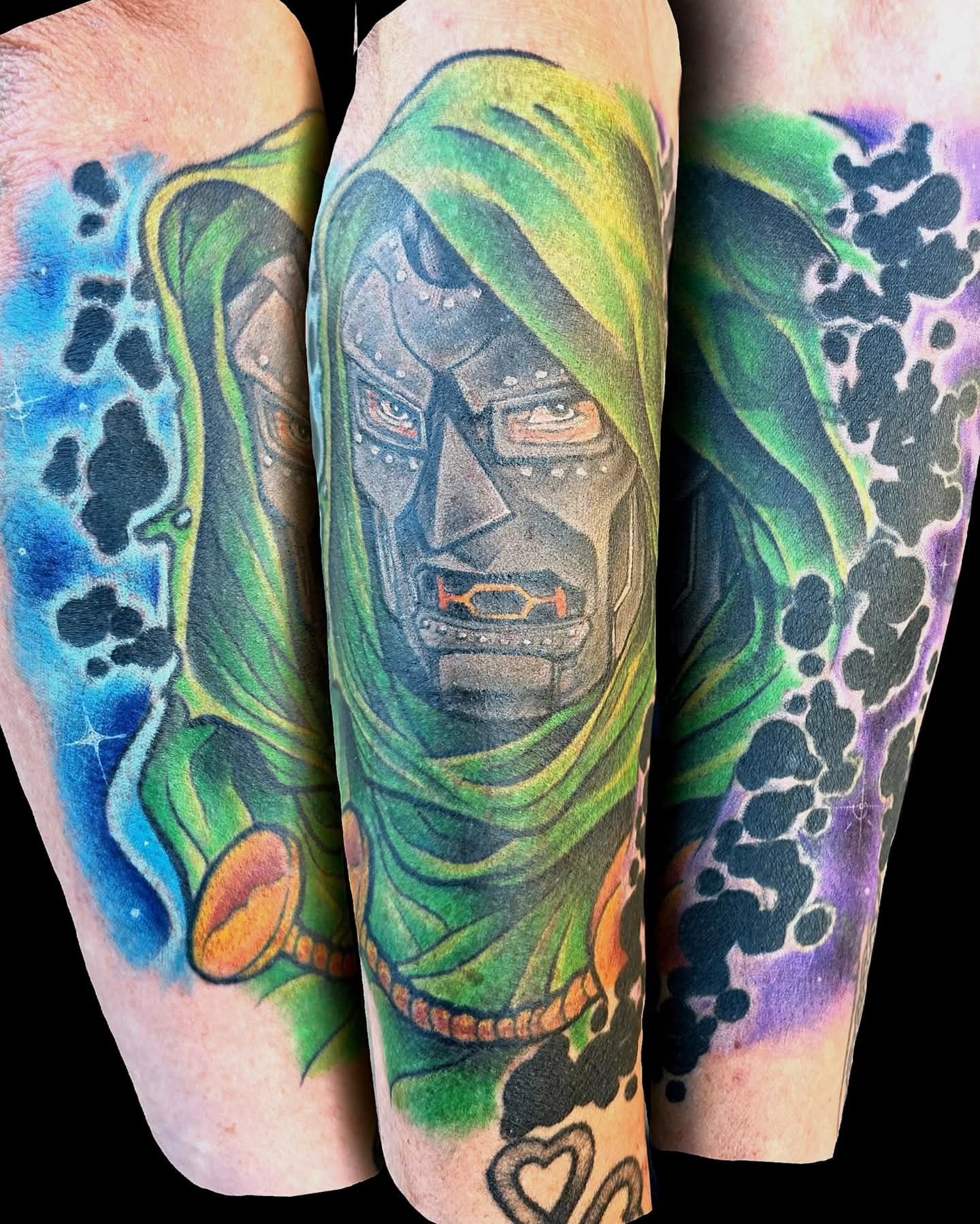 Tattoo of Doctor Doom's face with green hood and mask, set against colorful cosmic backgrounds.