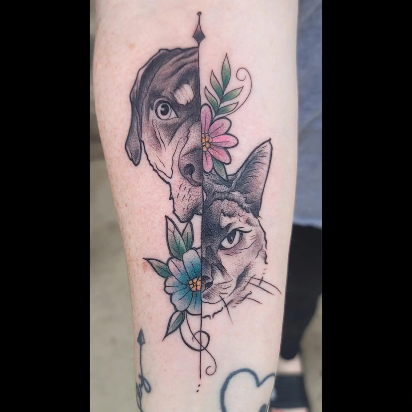Tattoo of a dog and a cat split vertically with flowers on the arm. The dog is brown/black. The cat is gray.