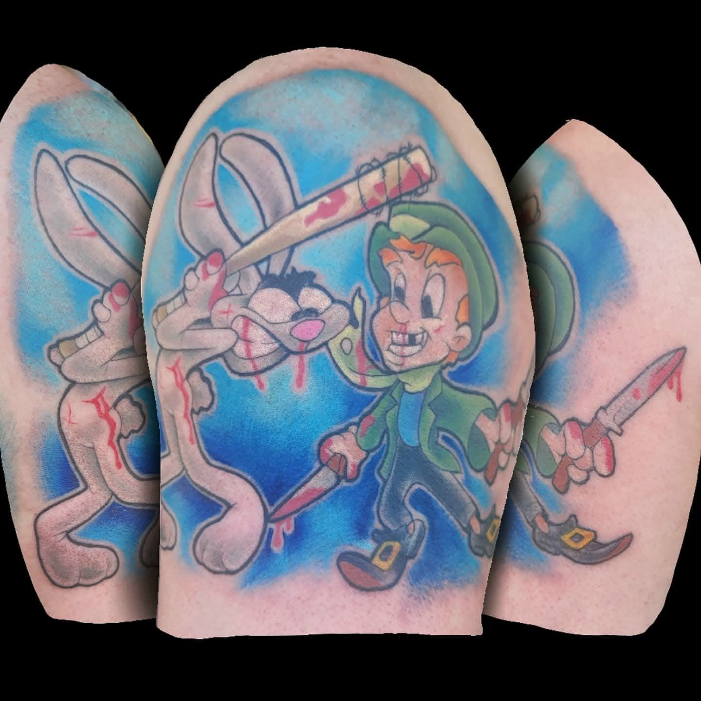 Tattoo of Bugs Bunny being hit with a bat by Lucky the Leprechaun, with blood spatter, blue background.