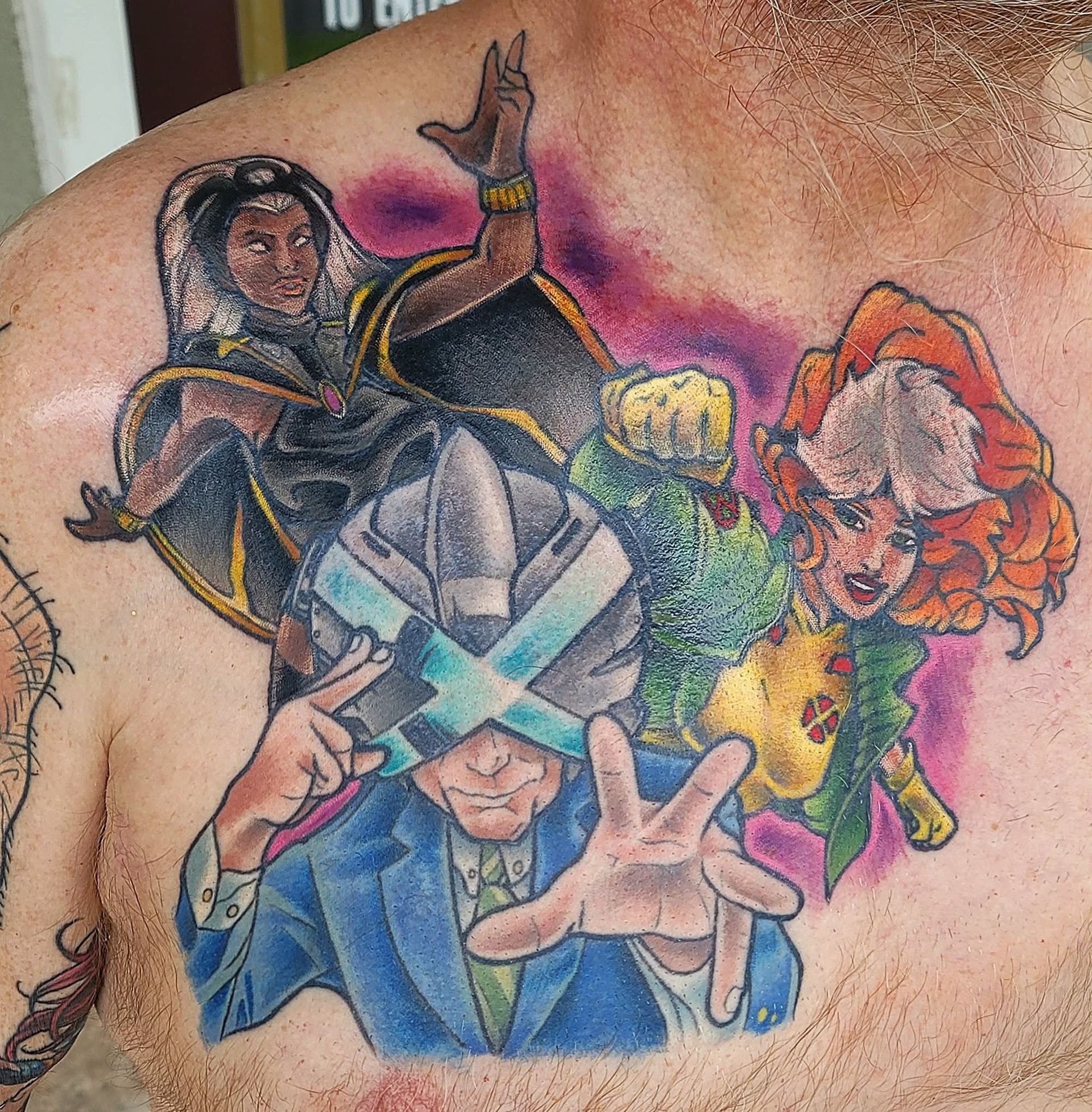 X-Men tattoo on chest: Storm, Rogue, and a Cyclops-like figure. Colorful art with a superhero theme.