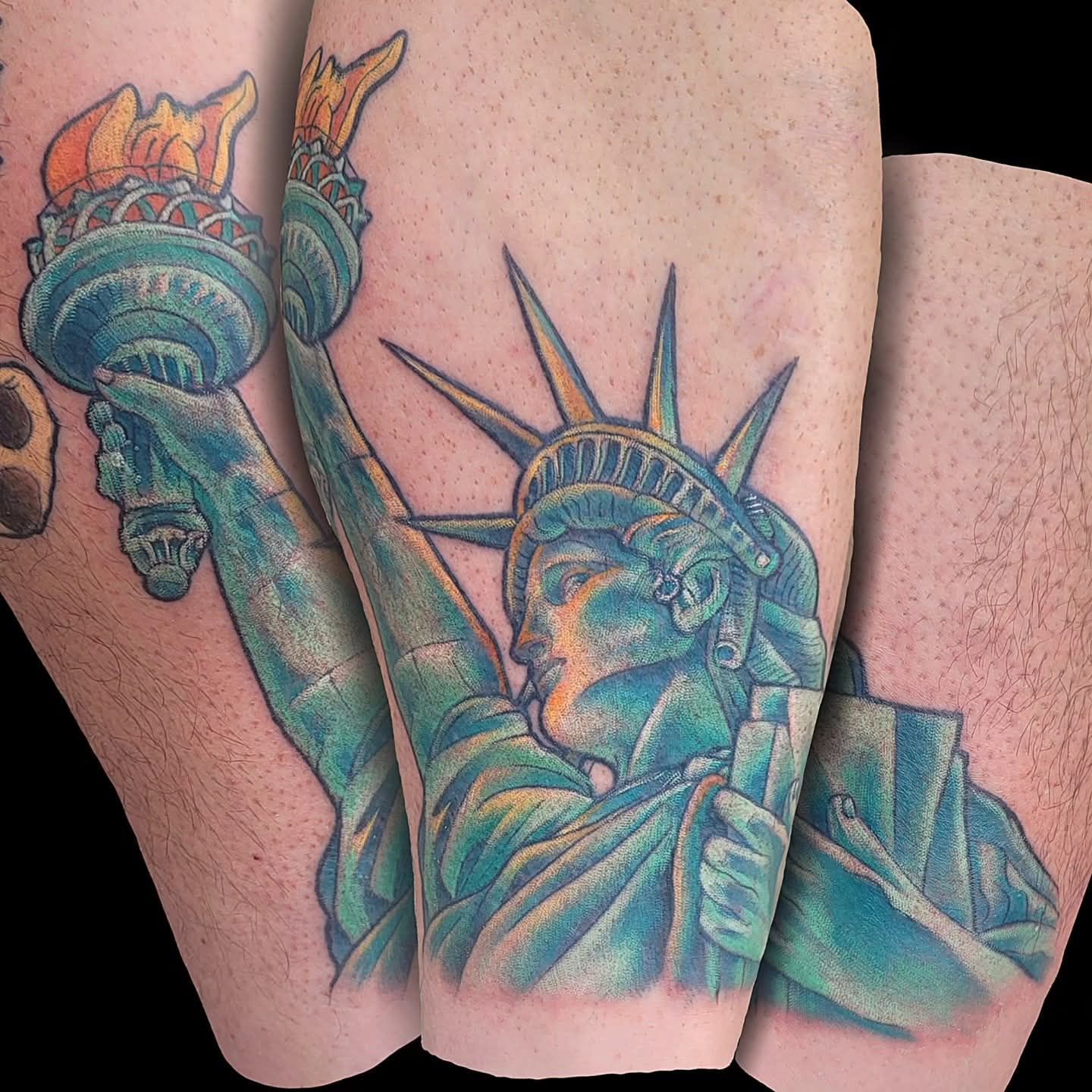 Tattoo of the Statue of Liberty on a leg. Turquoise with yellow flame and sun rays, black background.