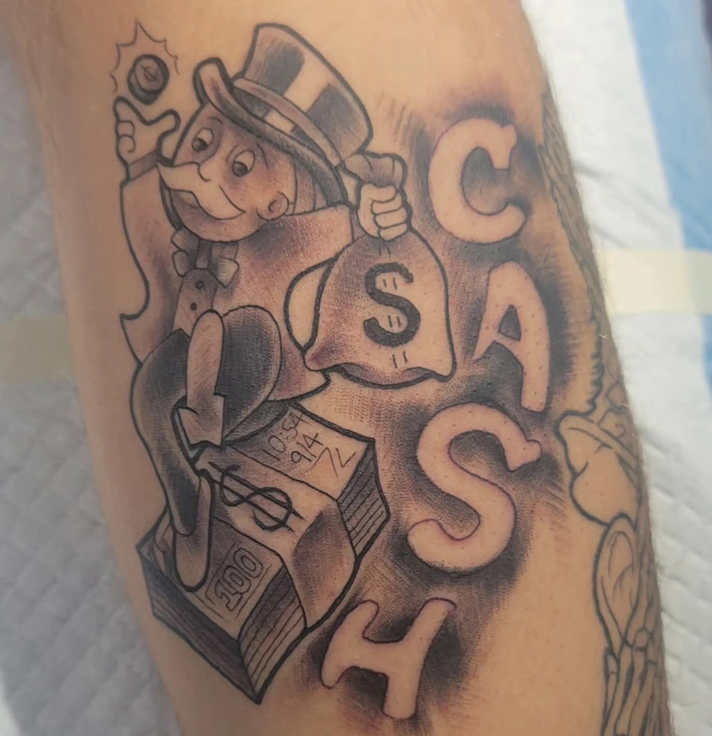 Monopoly Man tattoo with money bag, cash text, and $ bills.