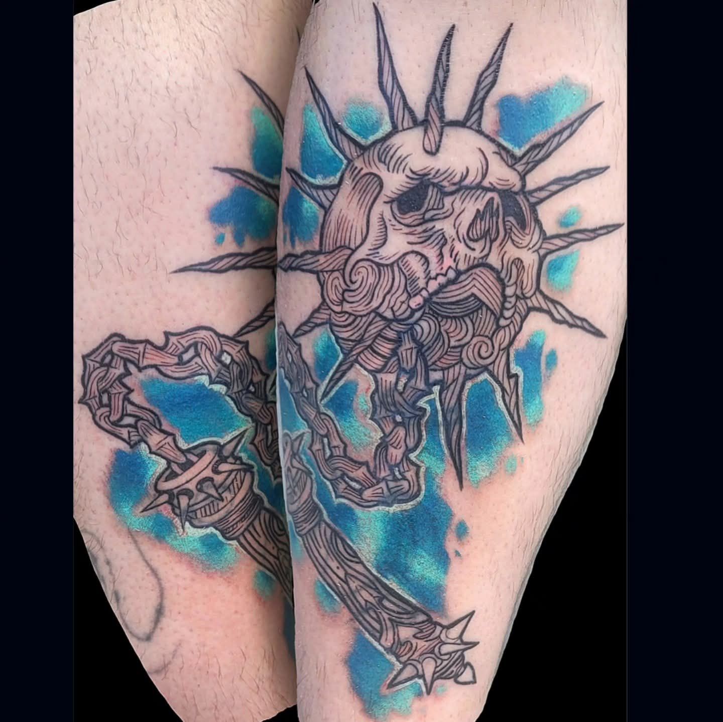 Tattoo of a skull with spiked crown, flail, and blue background on a person's leg.