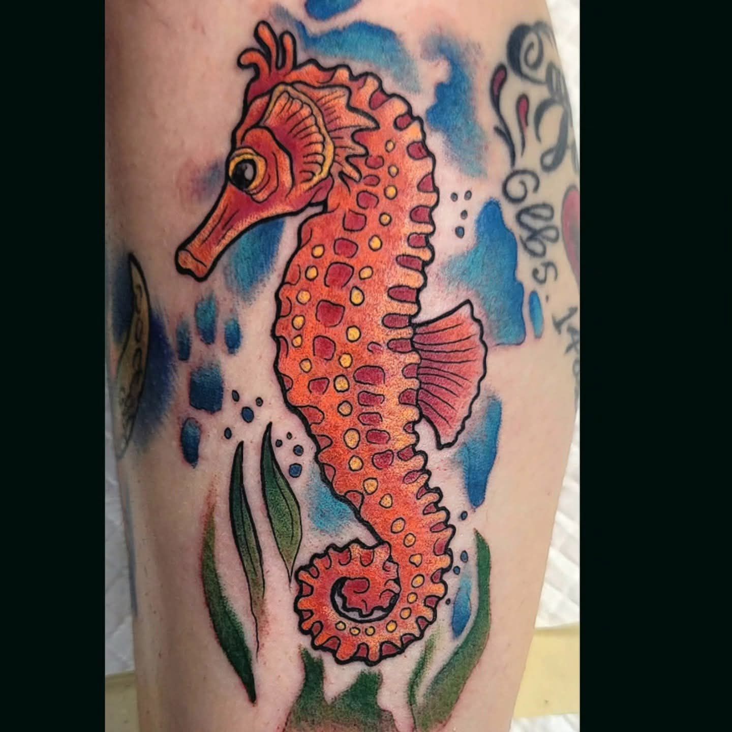 Orange seahorse tattoo with blue accents, green seaweed, and yellow highlights.