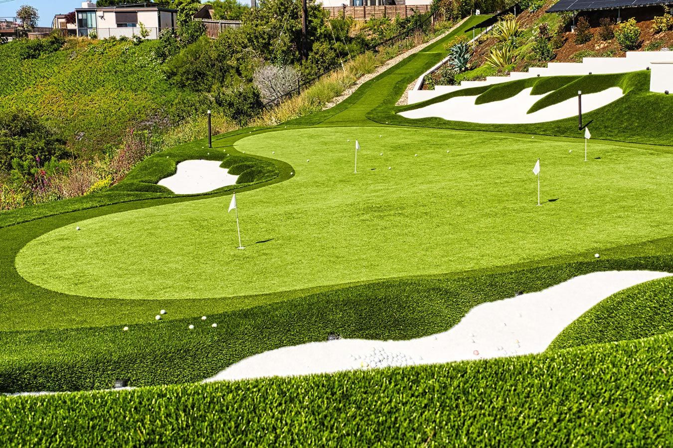 A golf course with a green and a white bunker on a hillside.