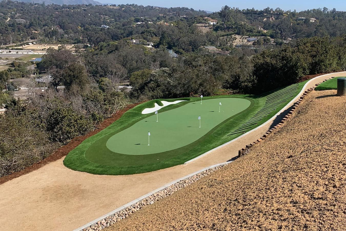 An aerial view of a golf course with trees in the background.