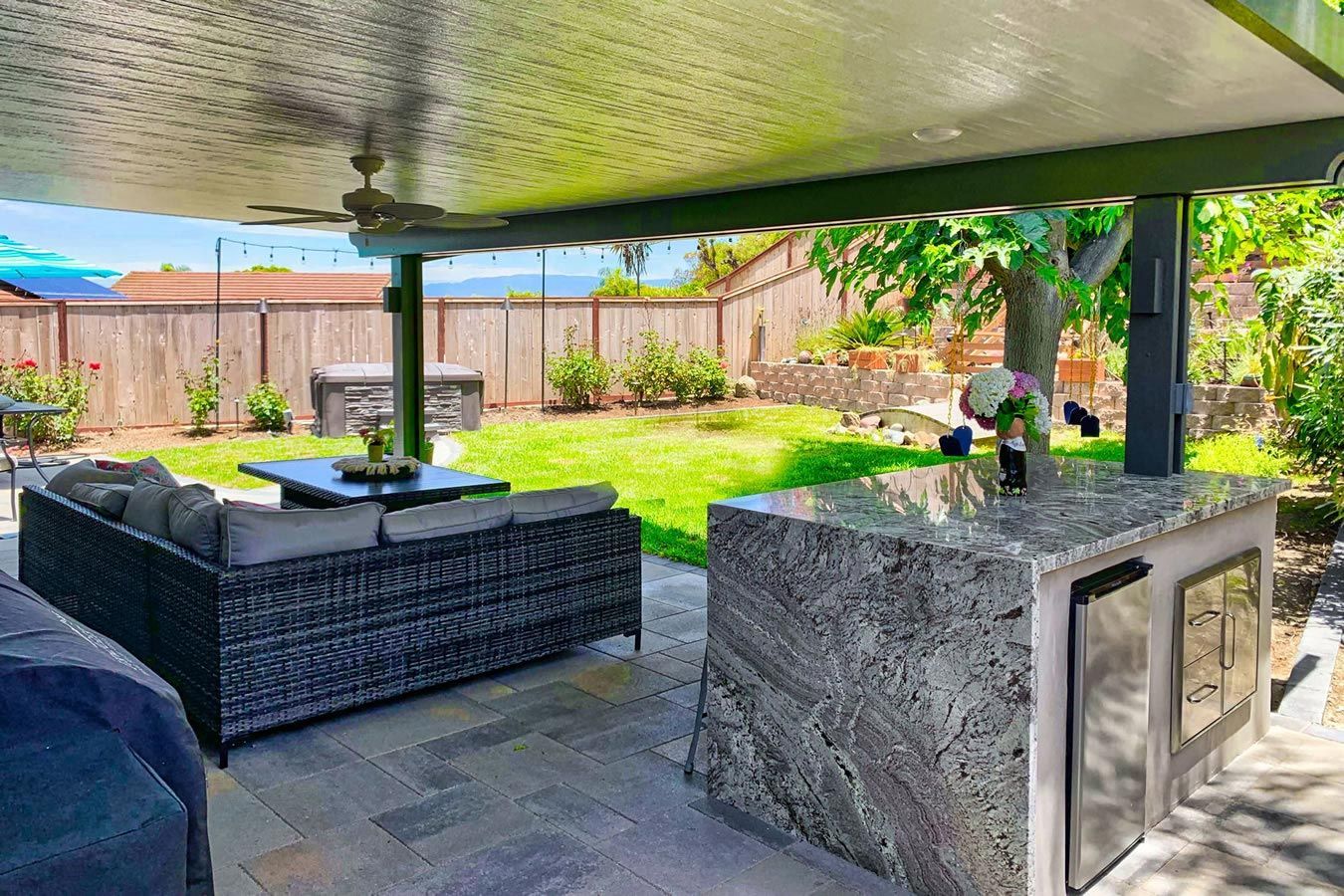A patio with a couch , table , and a kitchen in the backyard.