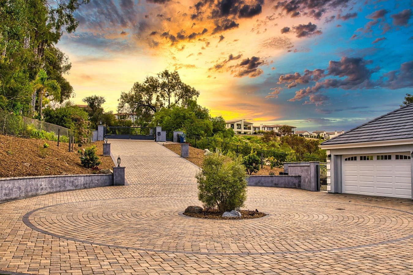 A brick driveway leading to a garage with a sunset in the background.