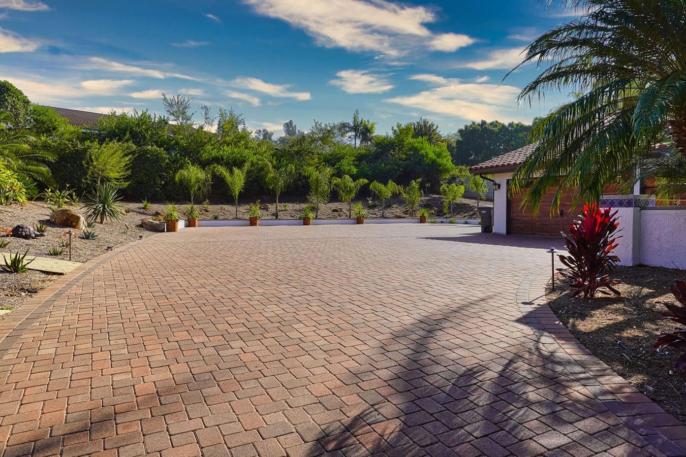 A brick driveway leading to a house with palm trees in the background