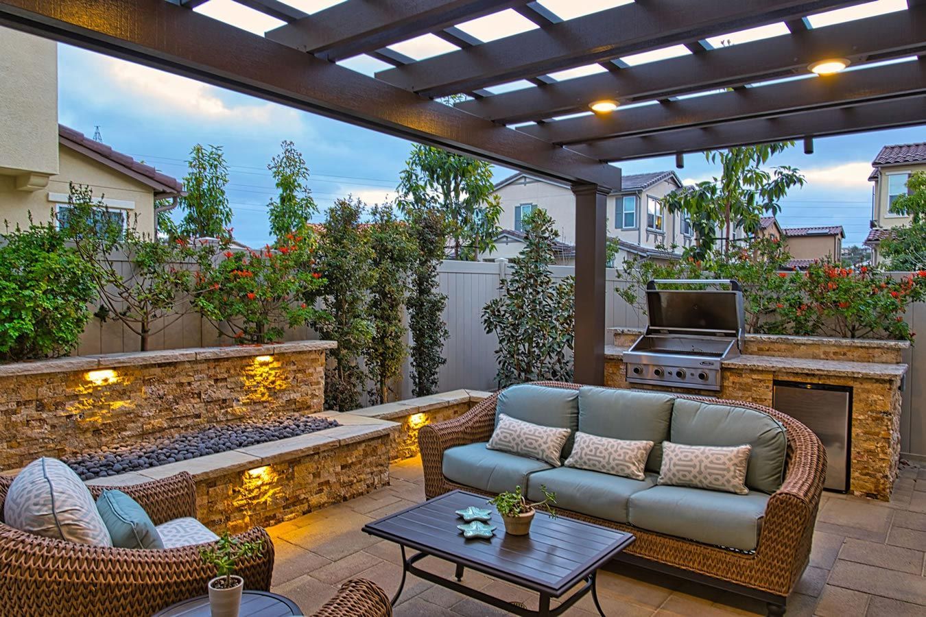 A patio with a couch , chairs , table and grill under a pergola.