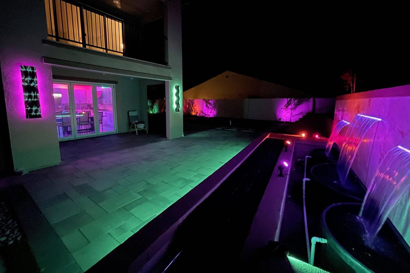 A waterfall is lit up at night in front of a house.