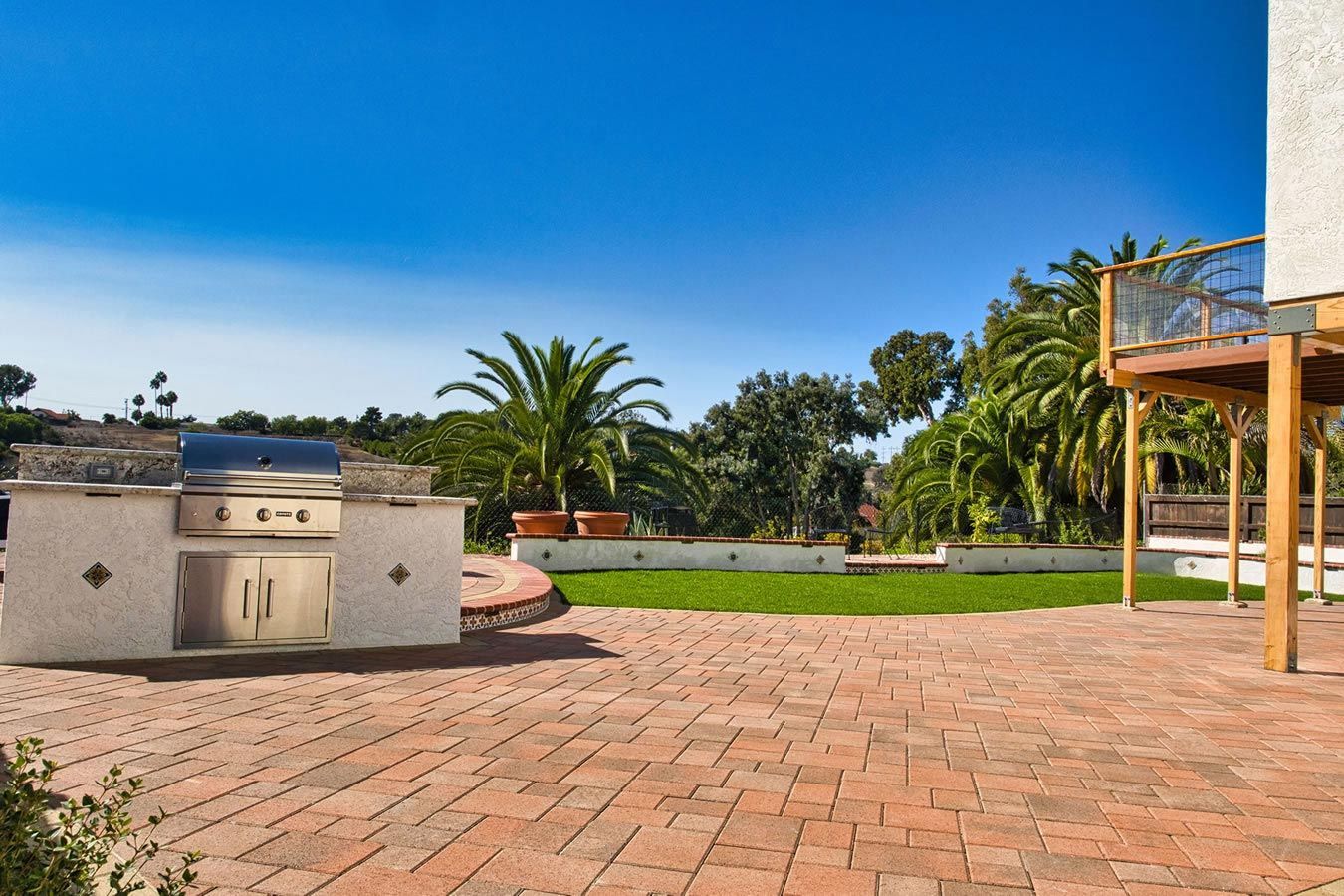 A brick patio with a grill and a deck in the background