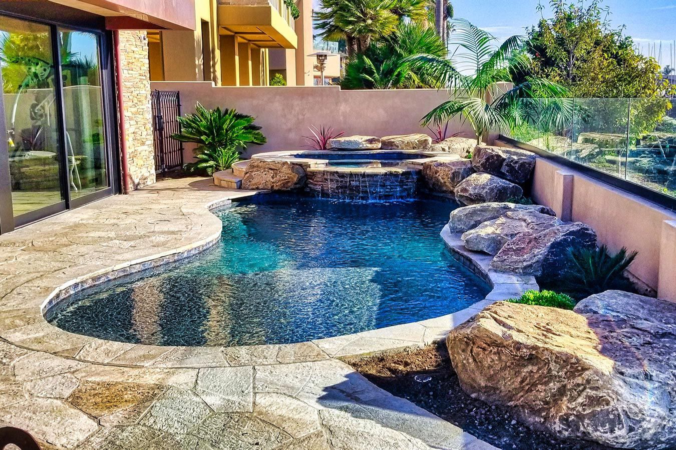 A large swimming pool surrounded by rocks and plants in a backyard.