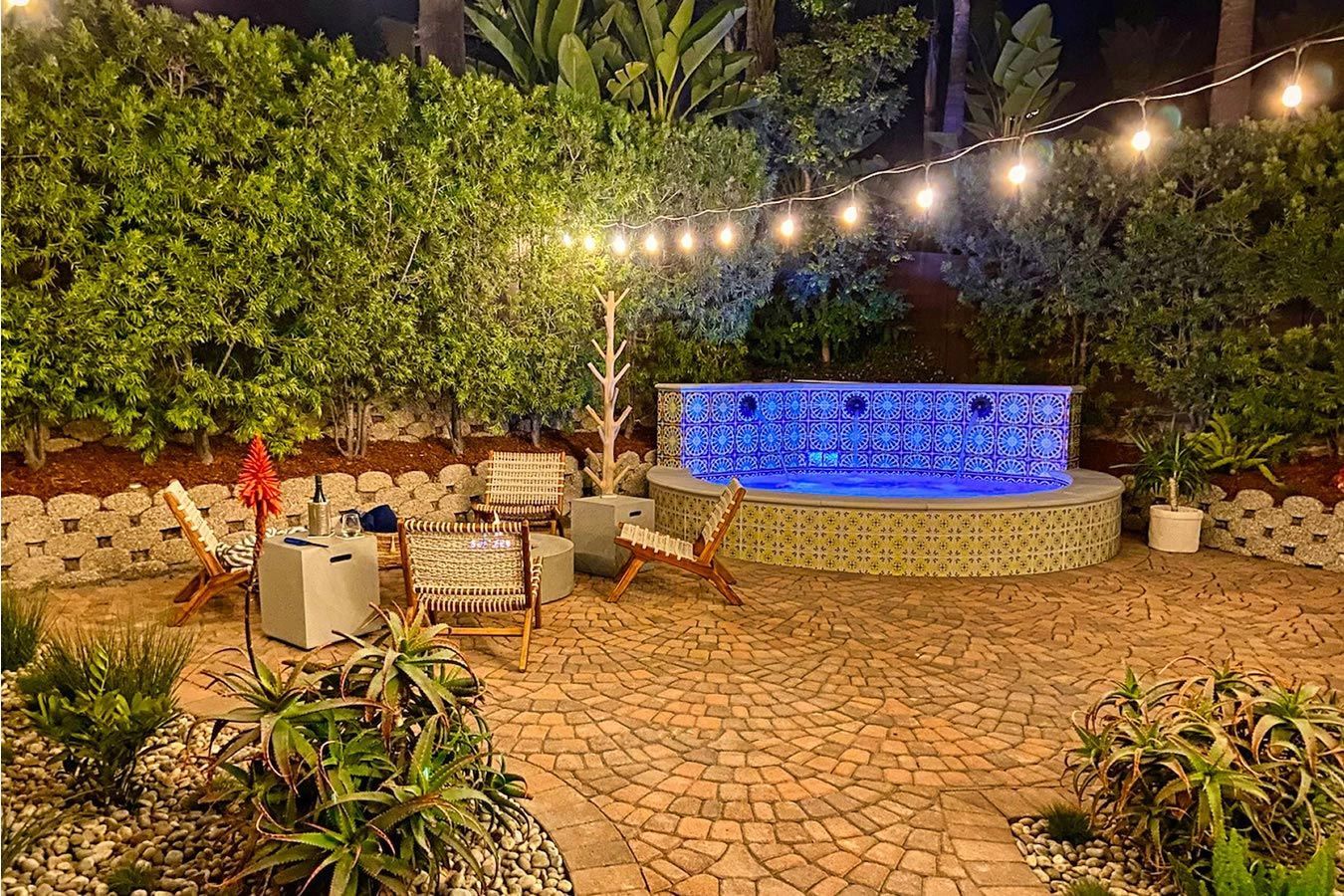 A patio with a pool and a fire pit at night.