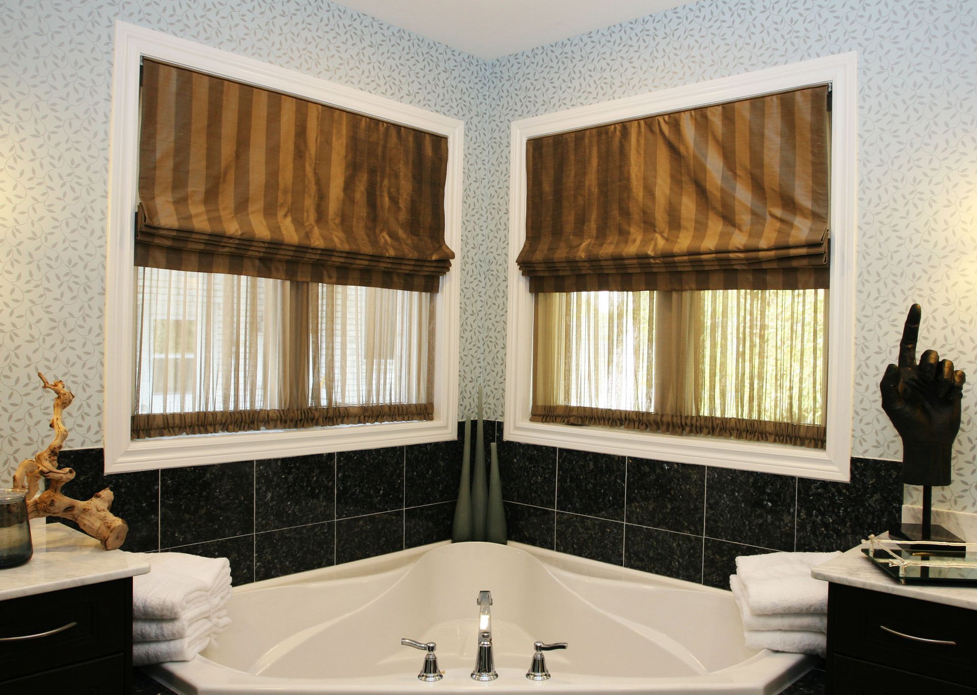 Corner bathtub with two windows, brown blinds, and dark tile trim in a bathroom