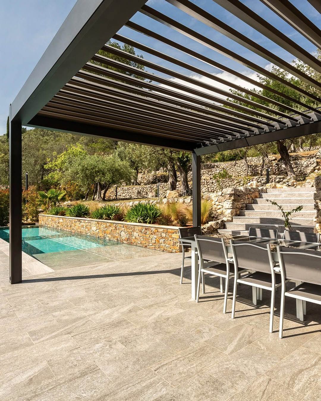 Outdoor patio with pergola, dining table, chairs, and a pool beside landscaped steps and desert plants