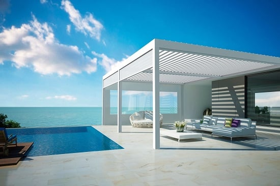 Modern seaside villa with infinity pool, white patio lounge, and ocean view under a bright blue sky