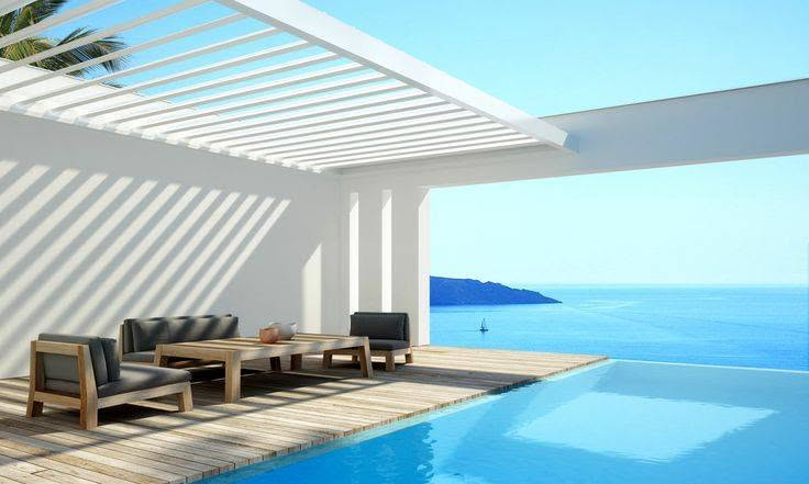 Modern patio with lounge chairs, pergola shade, and infinity pool overlooking a bright blue ocean