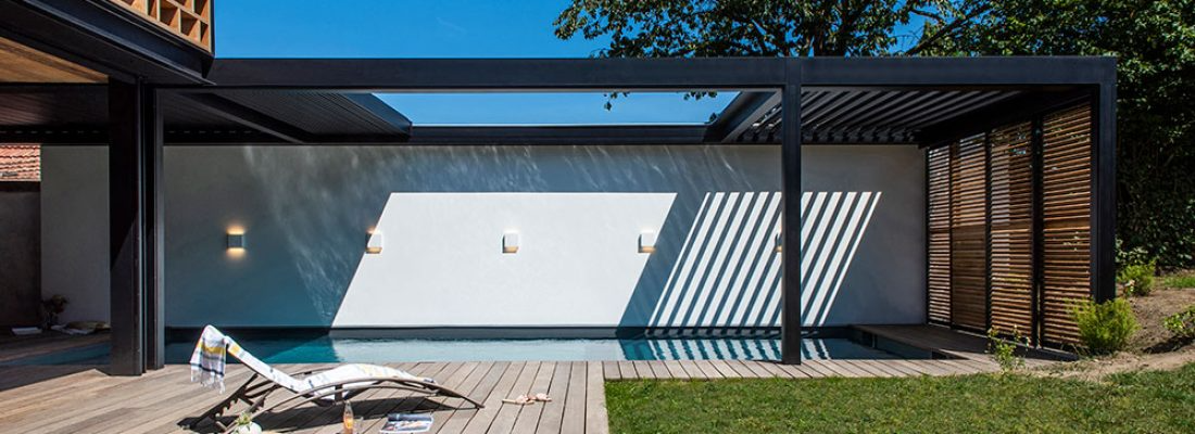 Modern backyard patio with a white wall, black pergola, and lounge chairs beside a pool