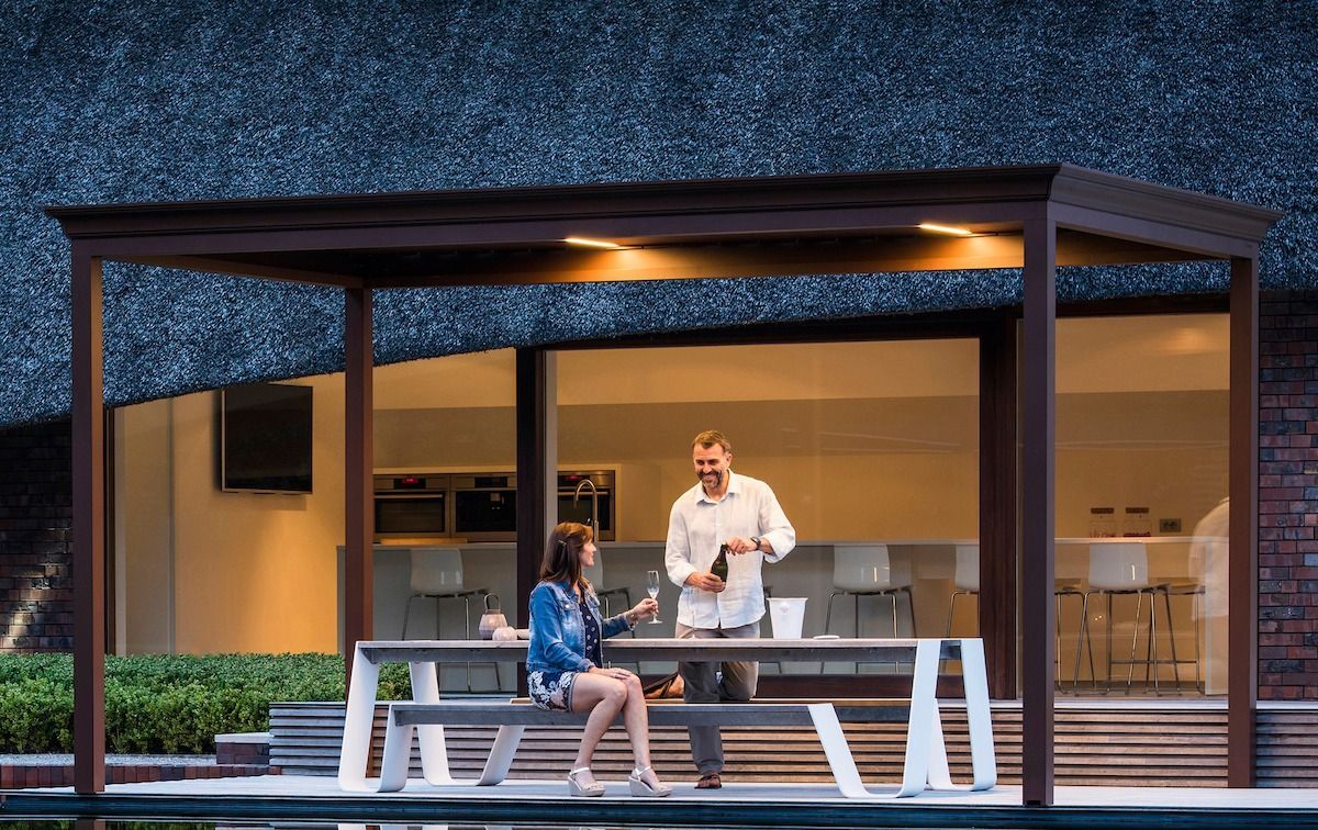 Two people on a bench in a lit outdoor pavilion at dusk, with warm interior lights behind them.