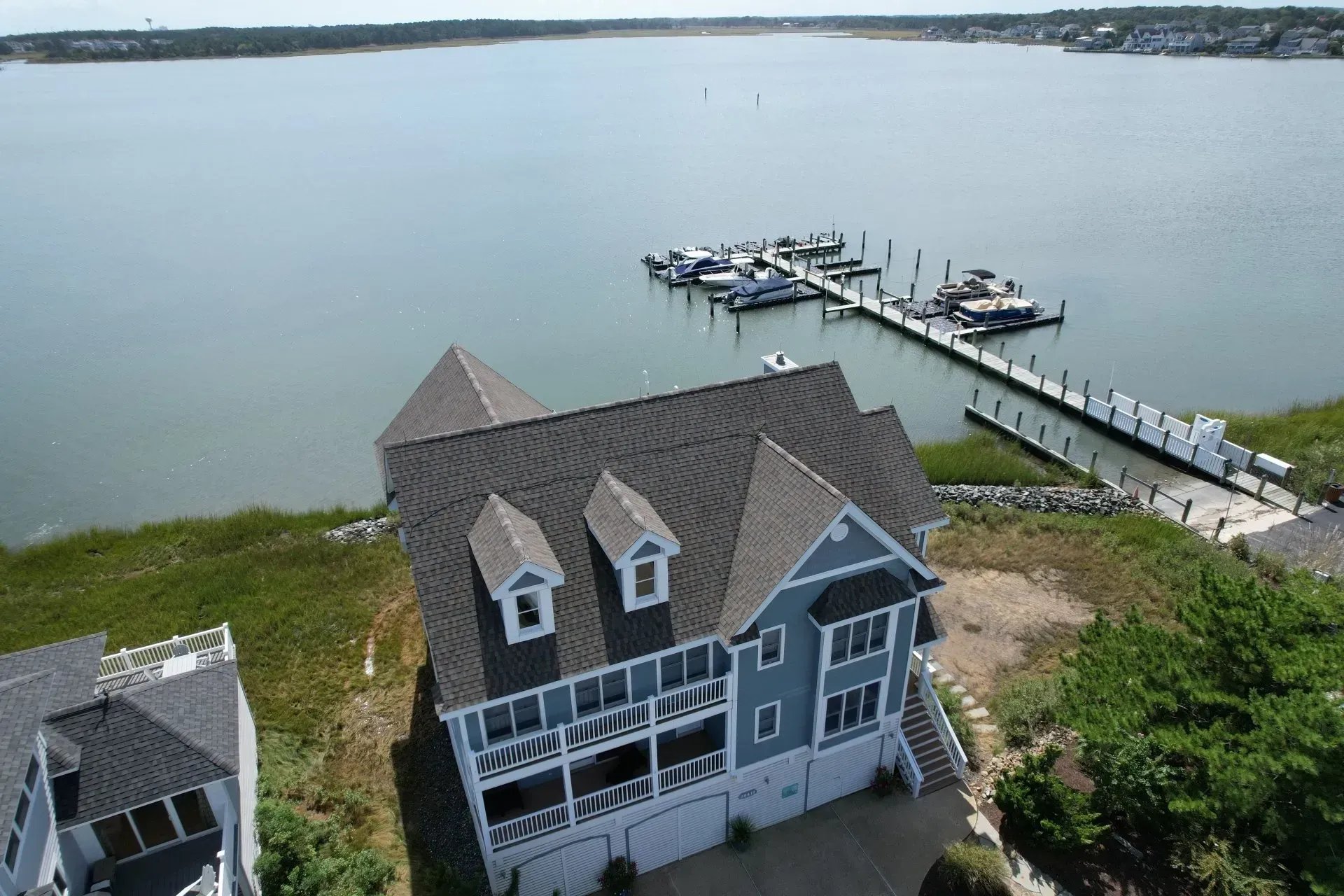 A gray waterfront house beside a dock on calm water, viewed from above.