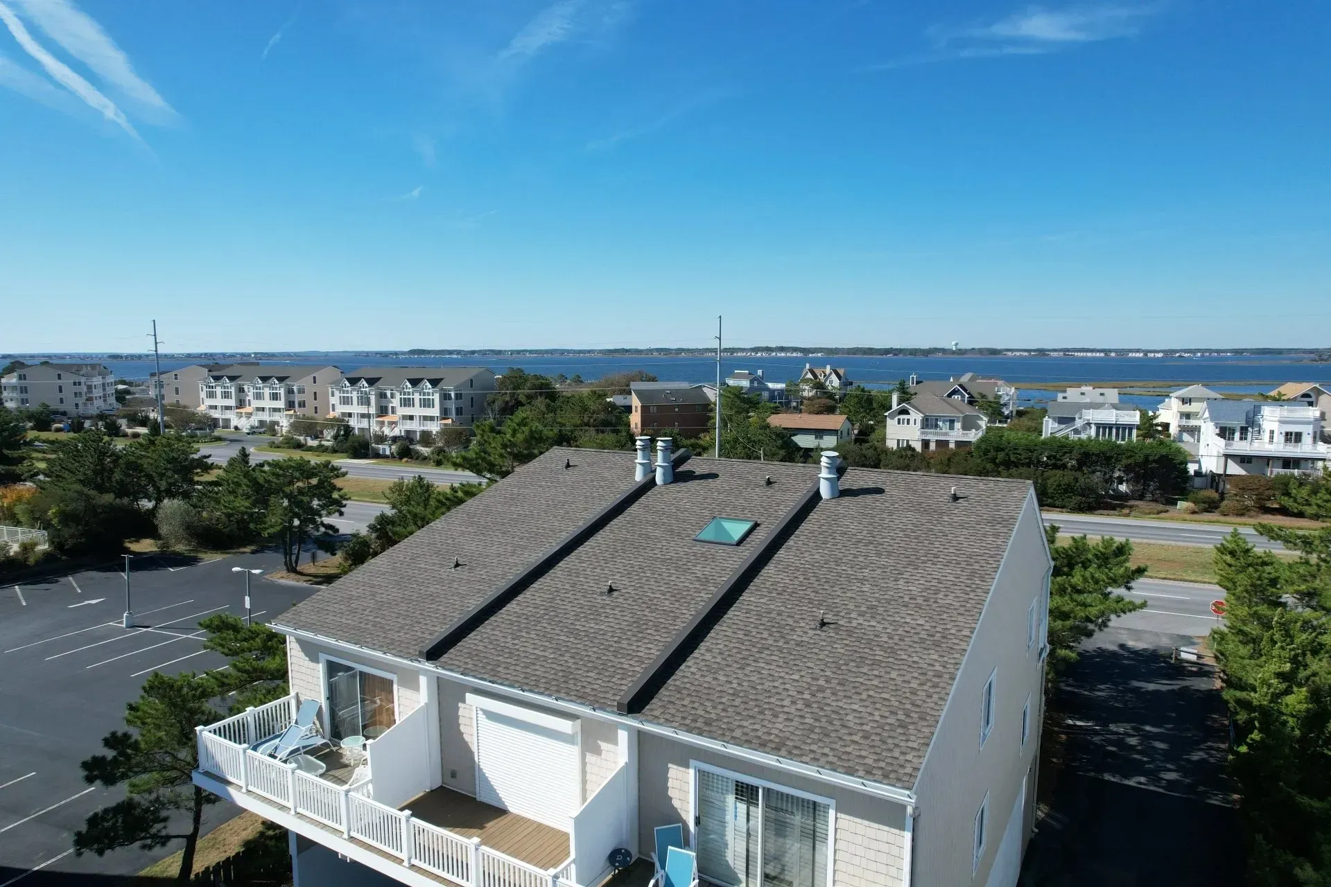Aerial view of a coastal neighborhood with a gray-roofed house, road, and ocean under a blue sky