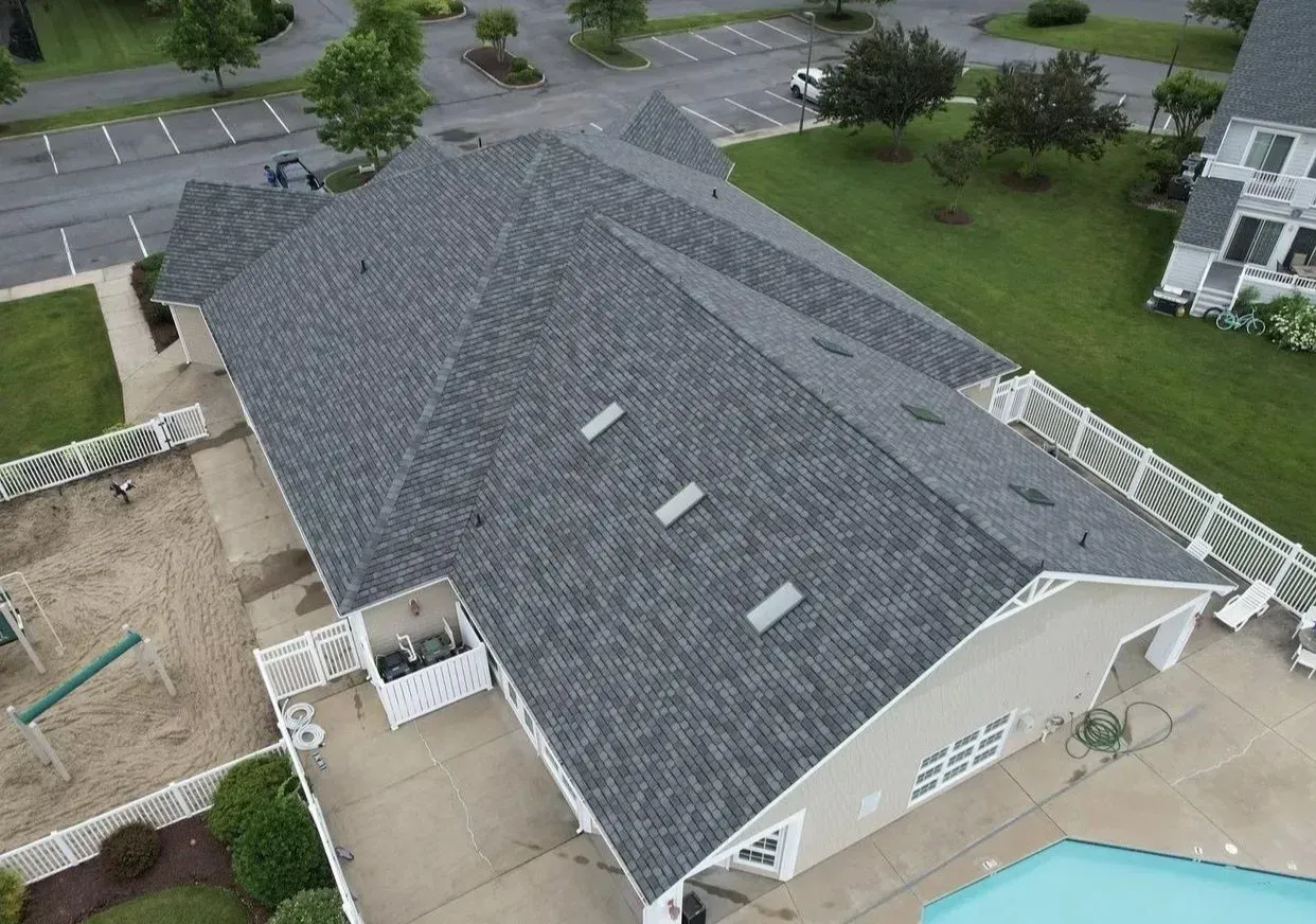 Aerial view of a gray-shingled house roof with skylights and a nearby backyard pool.