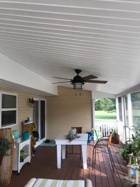 Covered porch with white table, chairs, and ceiling fan on a wooden deck.